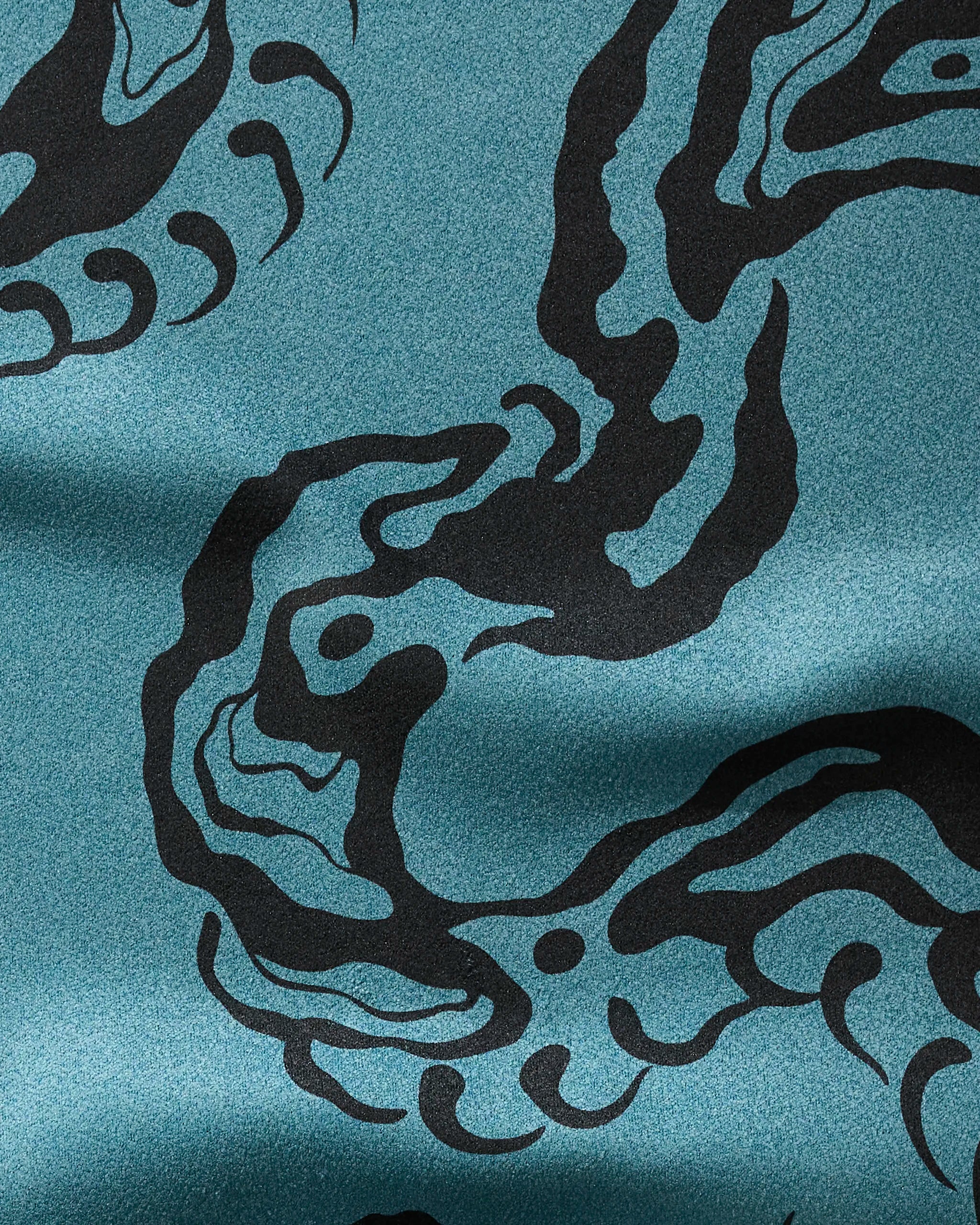 Close-up of the Cole Strem "Snake" fitness towel in teal, made from recycled materials. Features a black abstract swirling pattern like waves or tentacles, with a slightly shiny texture and gentle folds. Ultra-absorbent design.