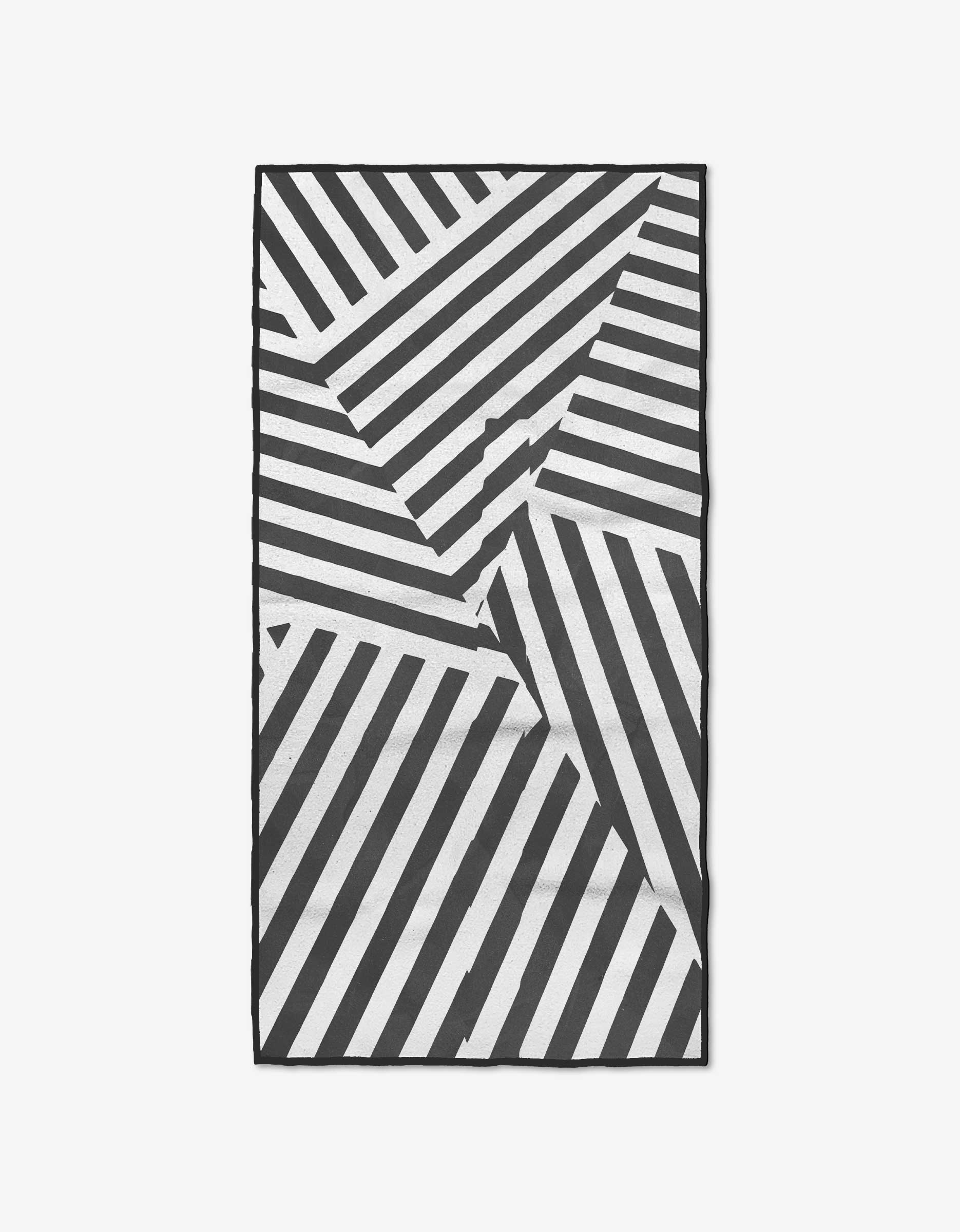 The Stripe and Stride rug by GEOMETRY features bold black and white geometric stripes, crafted from post-consumer recycled materials for a modern, eco-friendly touch. One corner of the rectangular rug is slightly folded.
