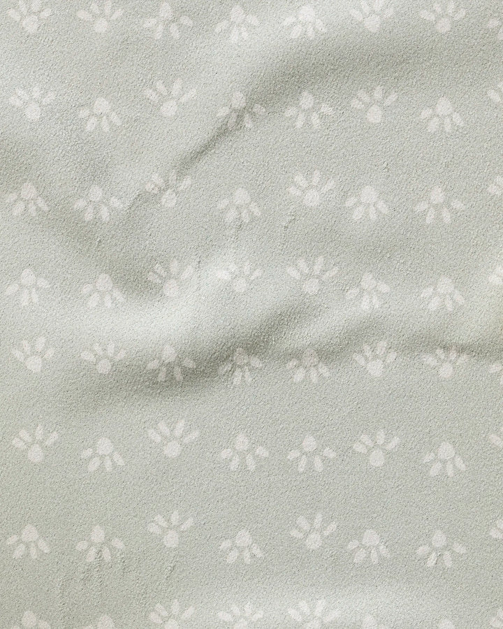 The Sun Bursts towel by Anee Shah is ultra-absorbent, light grey, and features a subtle small white paw print pattern with a slightly wrinkled, textured surface.