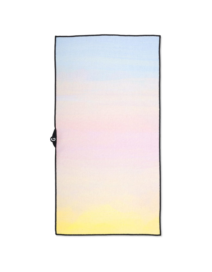 The GEOMETRY Magna - Sunrise is a rectangular fitness towel made from recycled materials, featuring a soft gradient from blue to yellow and a small black loop on one side.