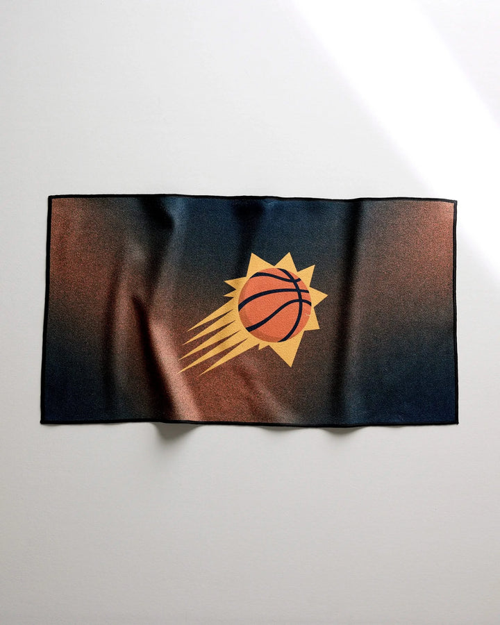 The NBALAB x Geometry Suns Fade towel is a rectangular, quick-dry gym towel featuring the Phoenix Suns logo with a stylized basketball and orange sunburst on a dark blue to copper gradient background, shown laid flat on a white surface.