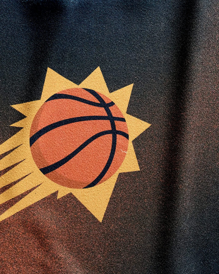 Close-up of the NBALAB x Geometry Suns Fade gym towel, showcasing the Phoenix Suns logo with a stylized basketball, motion lines, and a yellow sunburst on a dark quick-drying background.