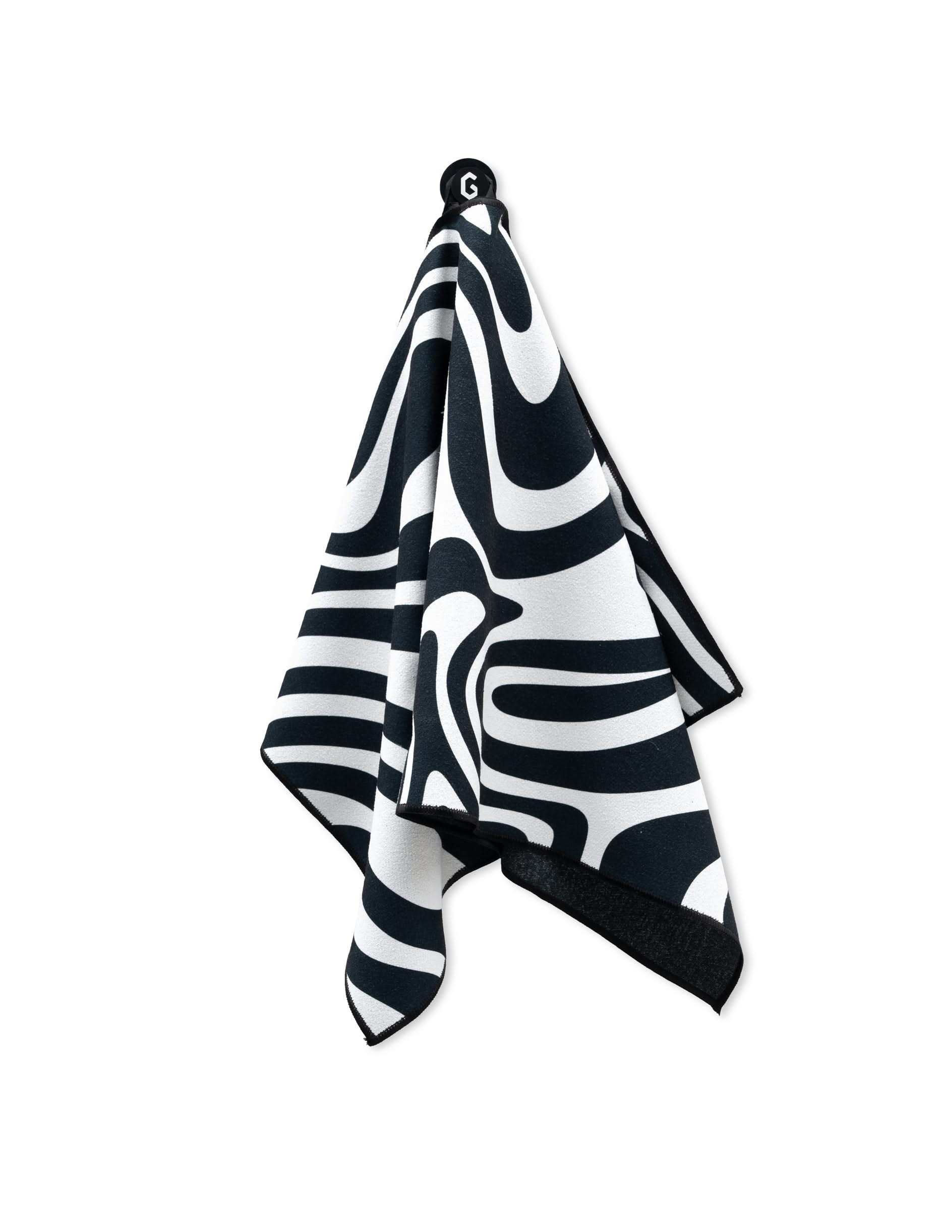 The GEOMETRY Magna - Swirls gym towel, featuring bold black and white wavy abstract patterns, hangs on a hook against a white background.