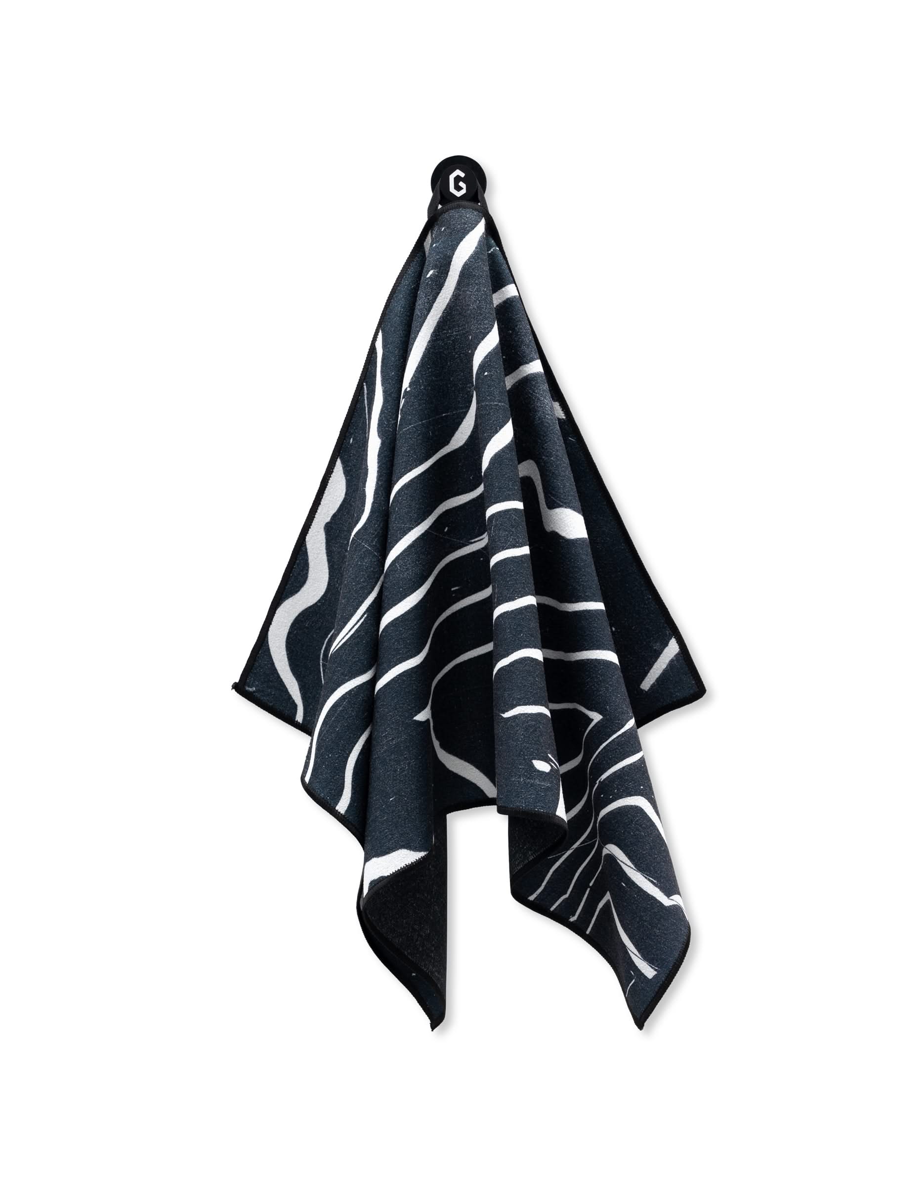 The GEOMETRY Magna - Ting is a black, ultra-absorbent gym towel featuring white abstract wavy lines, shown hanging from a small hook against a white background.