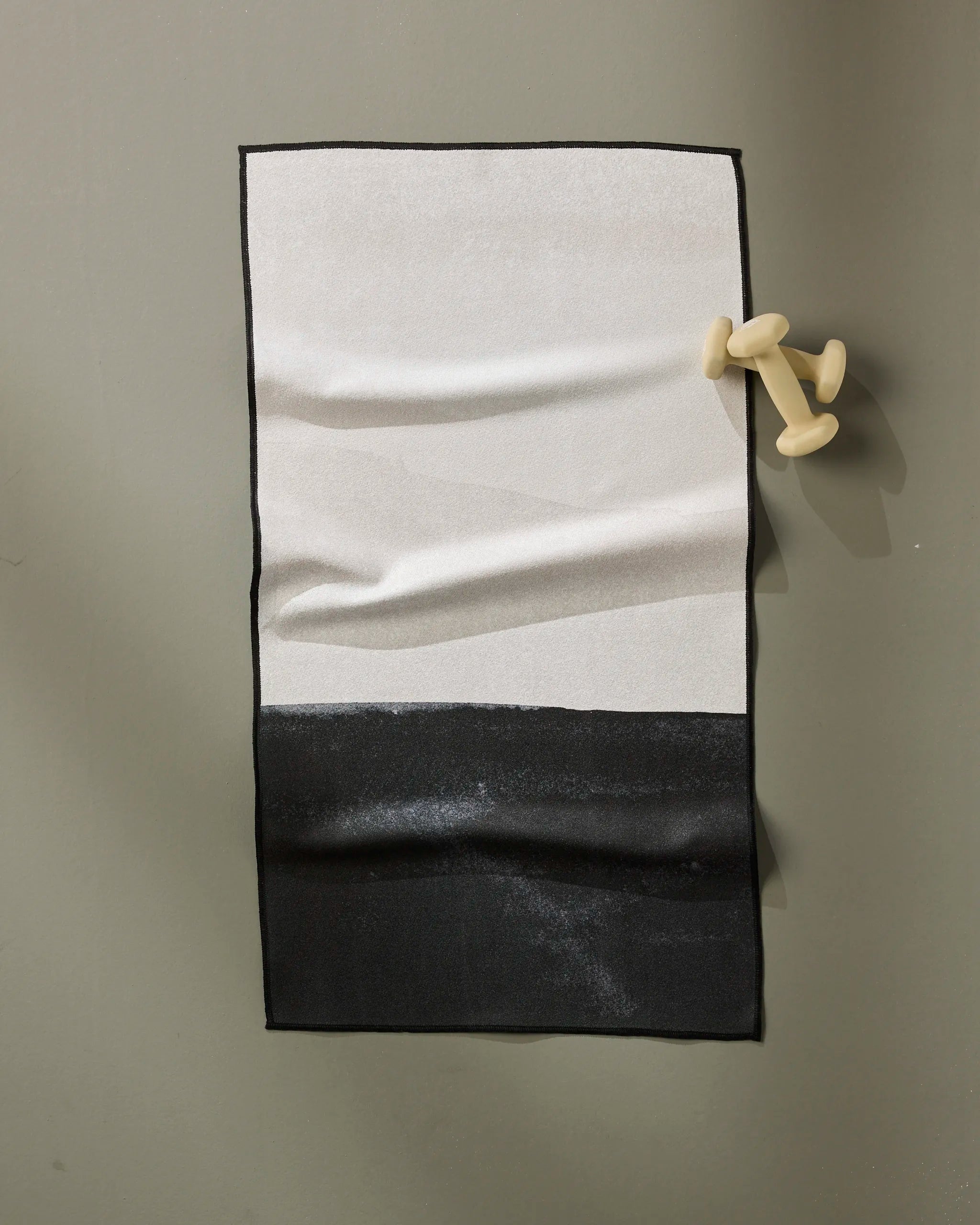 The Top Layer fitness towel by GEOMETRY features a sleek black and white color block design, displayed on a dumbbell-shaped modern hook. Crafted from ultra-absorbent, recycled materials for eco-friendly performance.