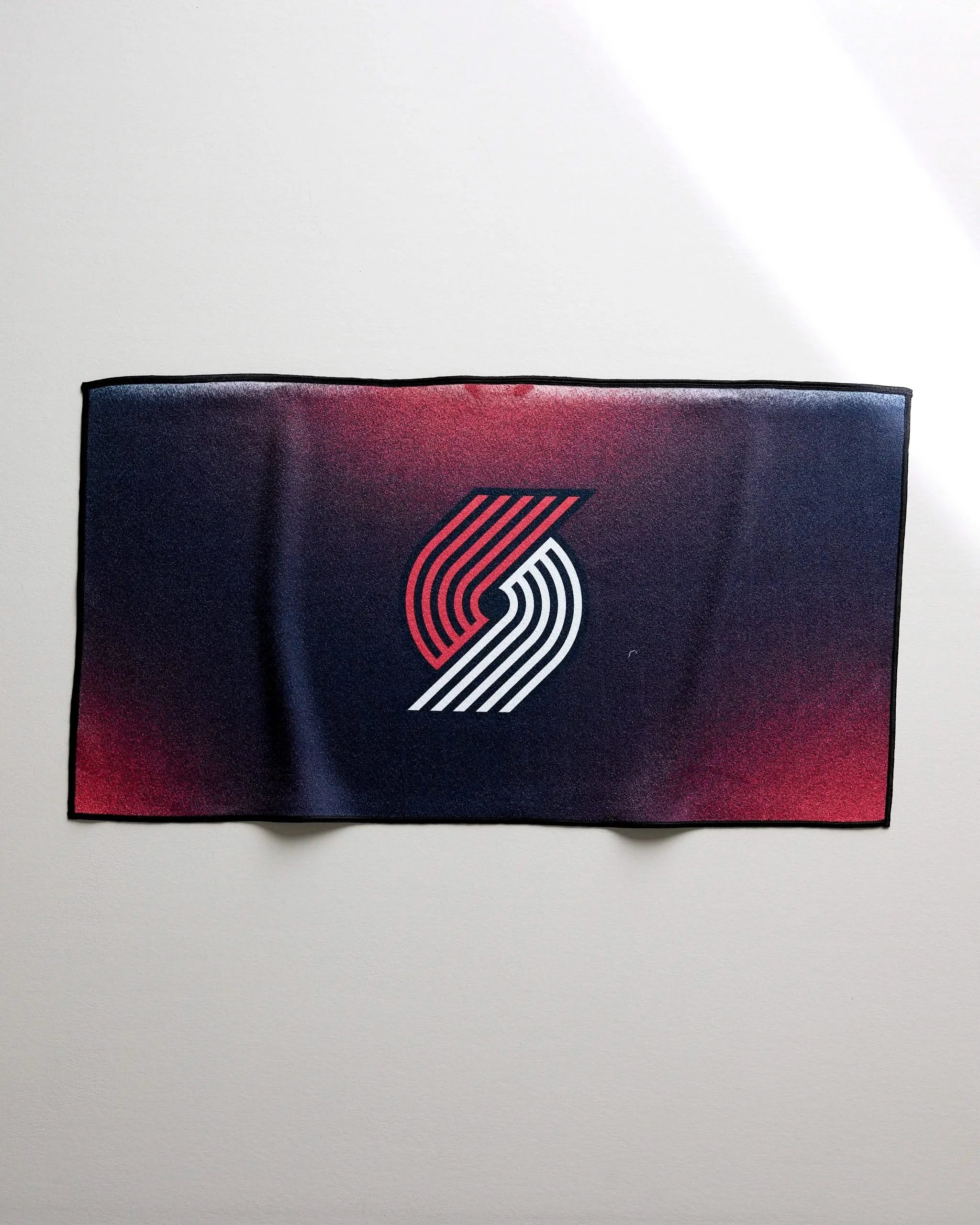 The NBALAB x Geometry Trail Blazers Fade is a rectangular, quick-drying gym towel with the team logo centered on a gradient background that transitions from dark red to black.