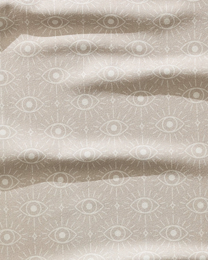 The Geometry Vision towel is a beige, ultra-absorbent fitness towel featuring a mystical repeating eye pattern with ray-like lines and gentle waves for texture. Quick-drying fabric ensures style and performance.