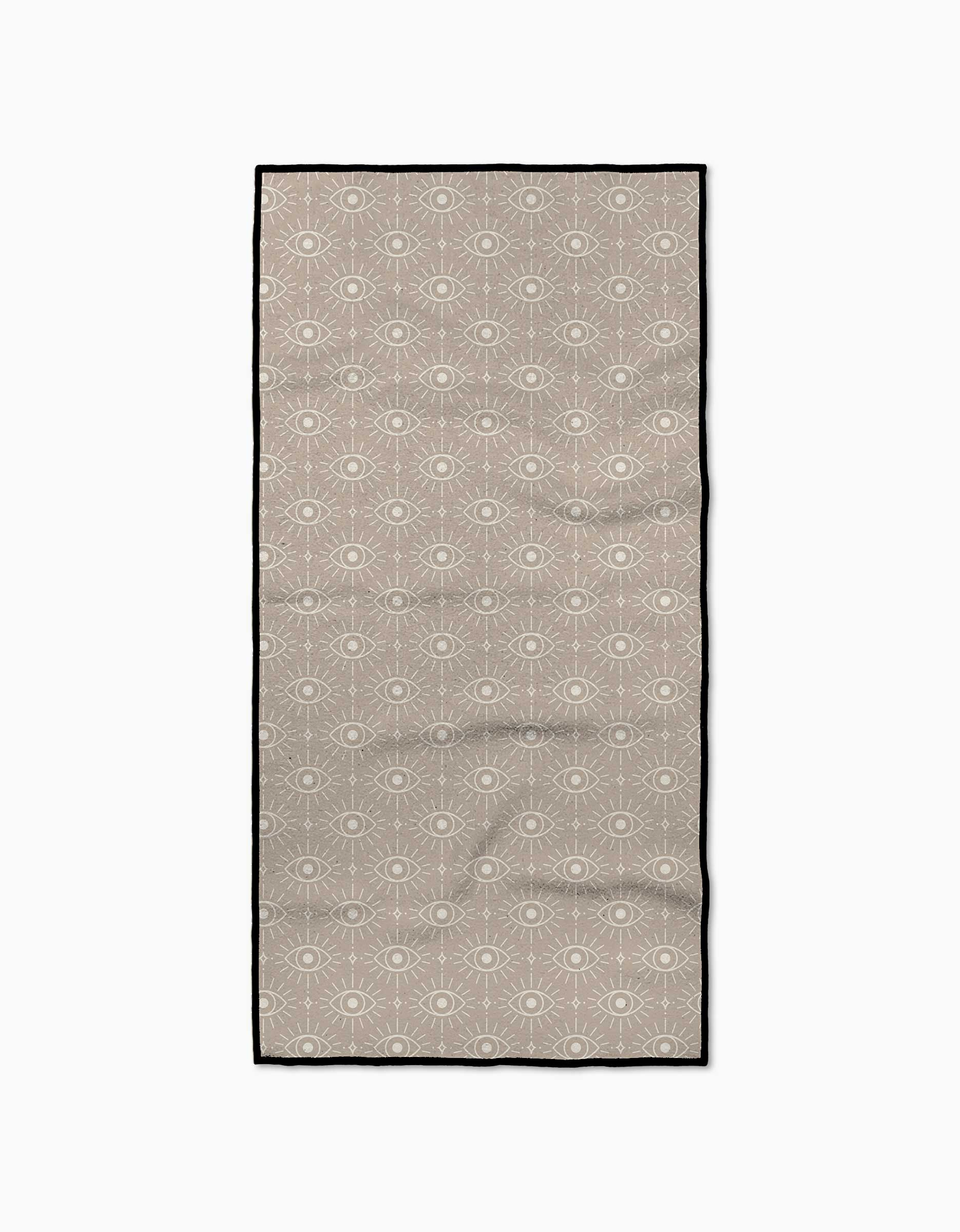 The Vision fitness towel by Geometry is a rectangular beige towel made from recycled materials, featuring a white eye pattern and a thin black border, shown on a plain white background.