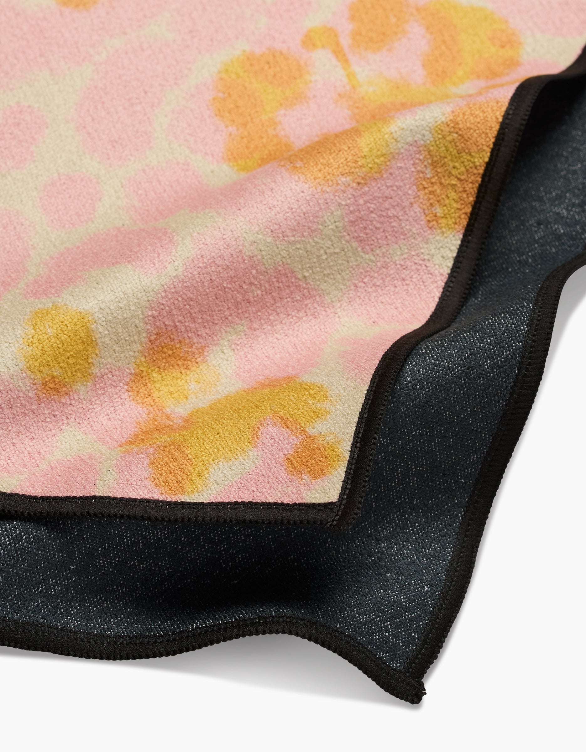 A close-up of GEOMETRY’s Whimsy: the top layer showcases a pink and yellow floral design made from recycled materials with a black edge, while the ultra-absorbent bottom fitness towel is solid black, also featuring a matching edge.