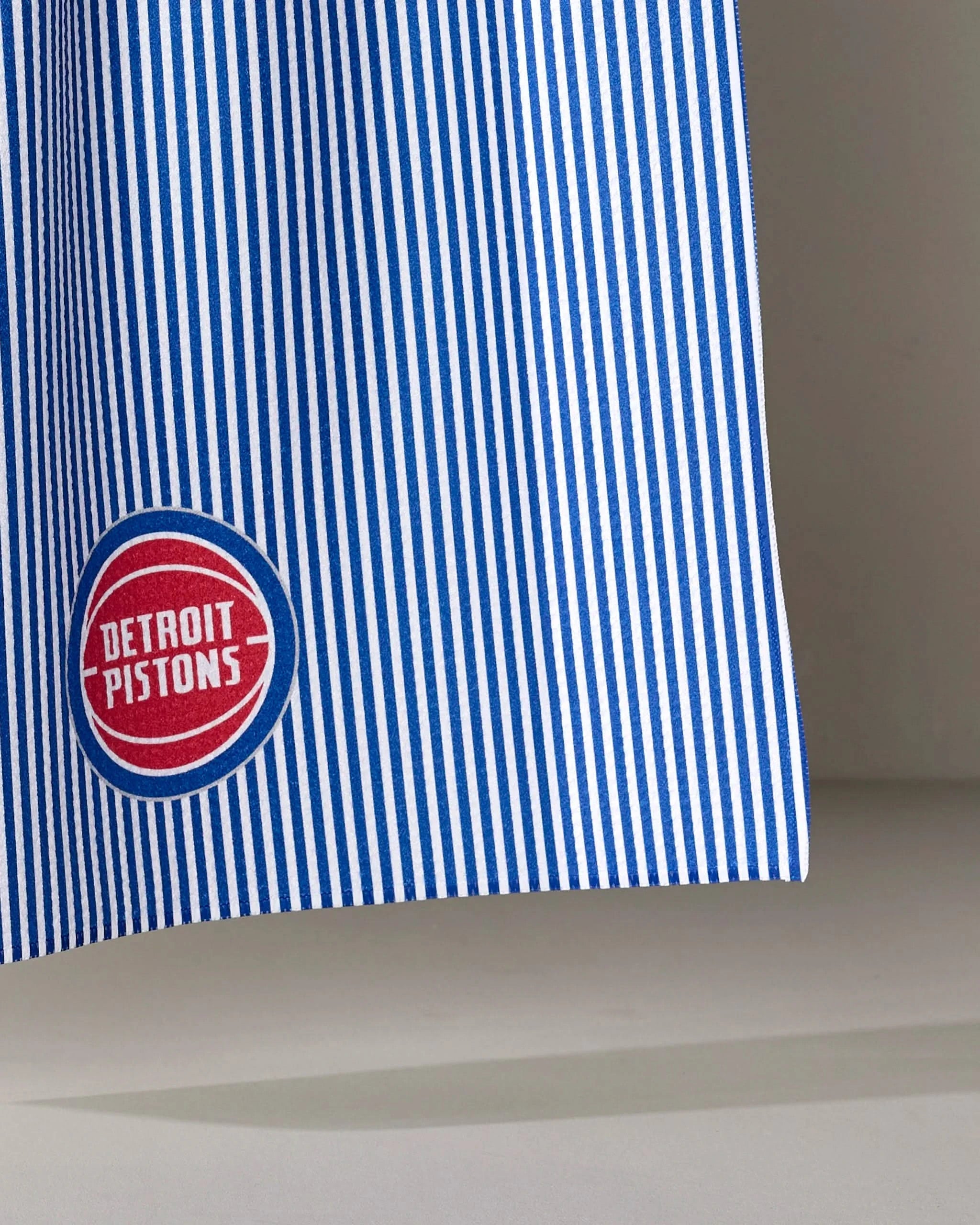 The Pistons Classic tea towel by NBALAB x Geometry features blue and white vertical stripes with a red and white Detroit Pistons logo patch—an officially licensed NBA design made for fans.