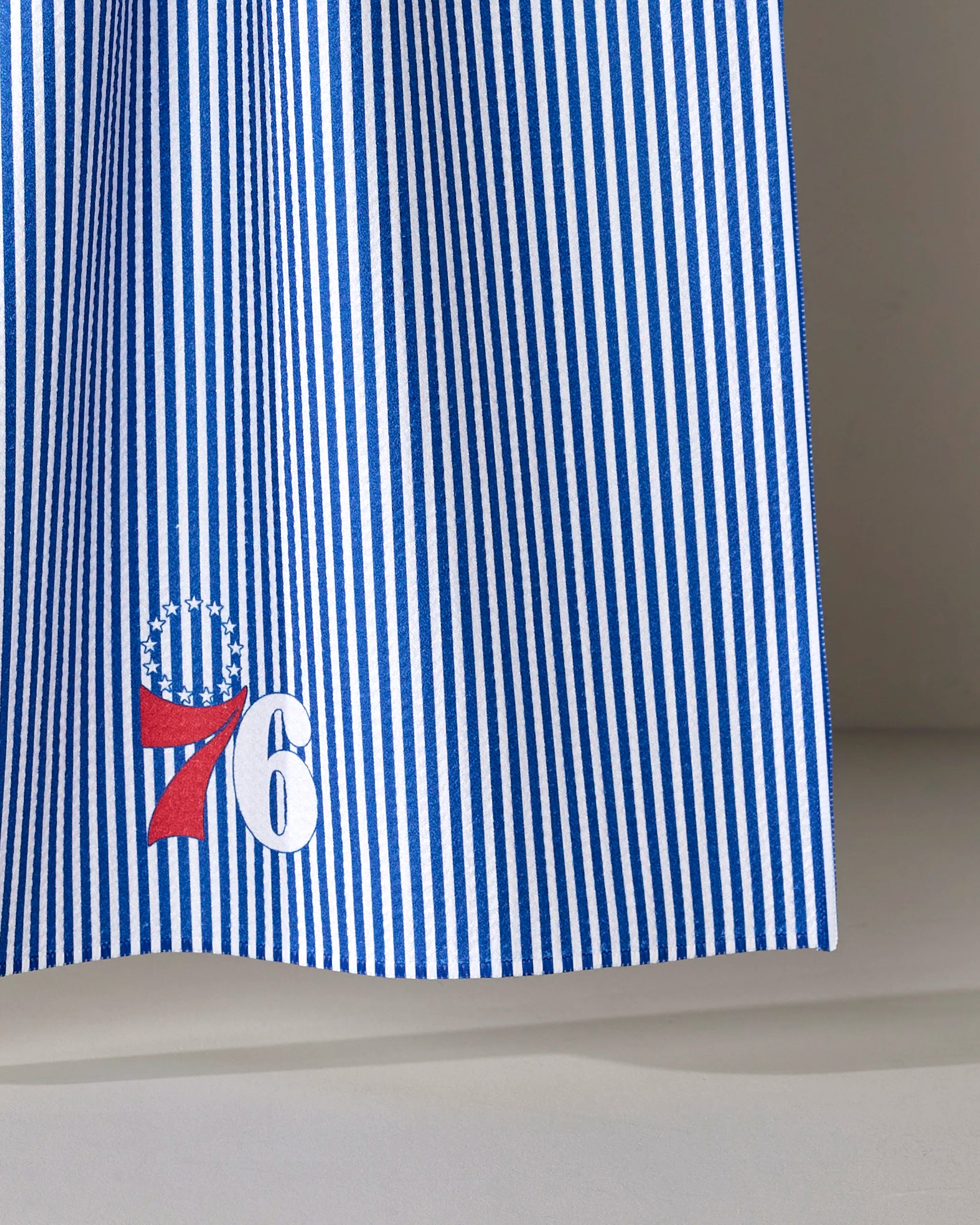 The 76ers Classic from NBALAB x Geometry is a sustainable kitchen towel with blue and white vertical stripes, featuring a red 7 and white 6 near the bottom topped by a circle of stars.