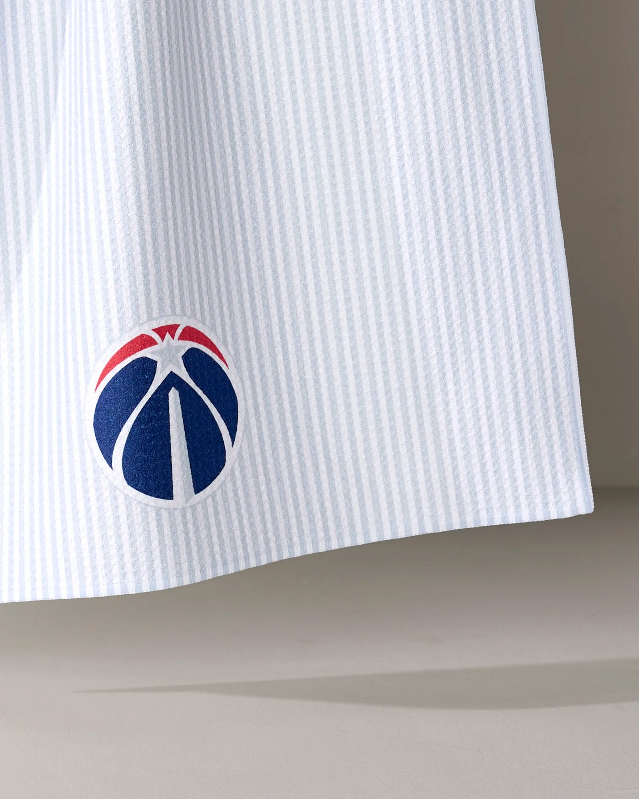 A close-up of the Wizards Classic tea towel by NBALAB x Geometry shows the Washington Wizards logo on white, vertically striped fabric with a blue basketball and red and white accents. Officially licensed NBA merchandise.