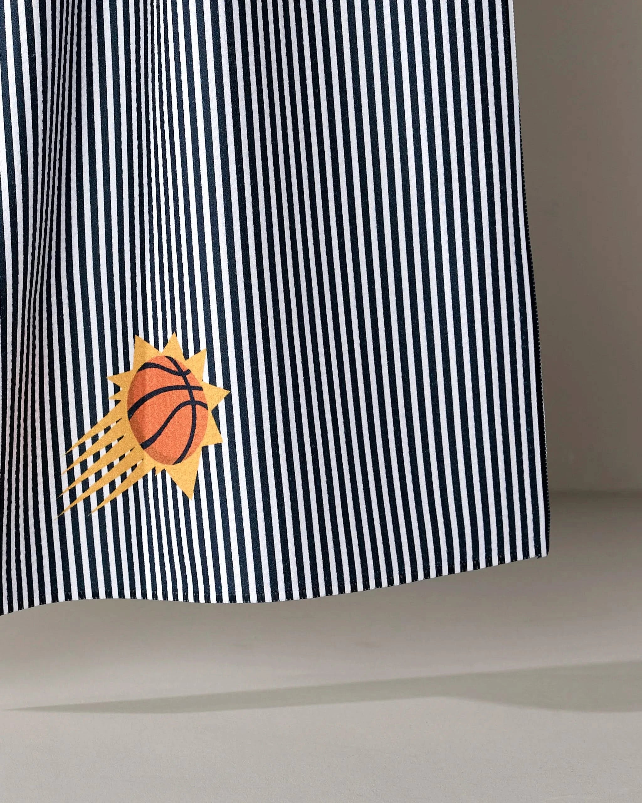 The Suns Classic tea towel by NBALAB x Geometry features black-and-white vertical stripes and a small Phoenix Suns logo printed near the bottom.