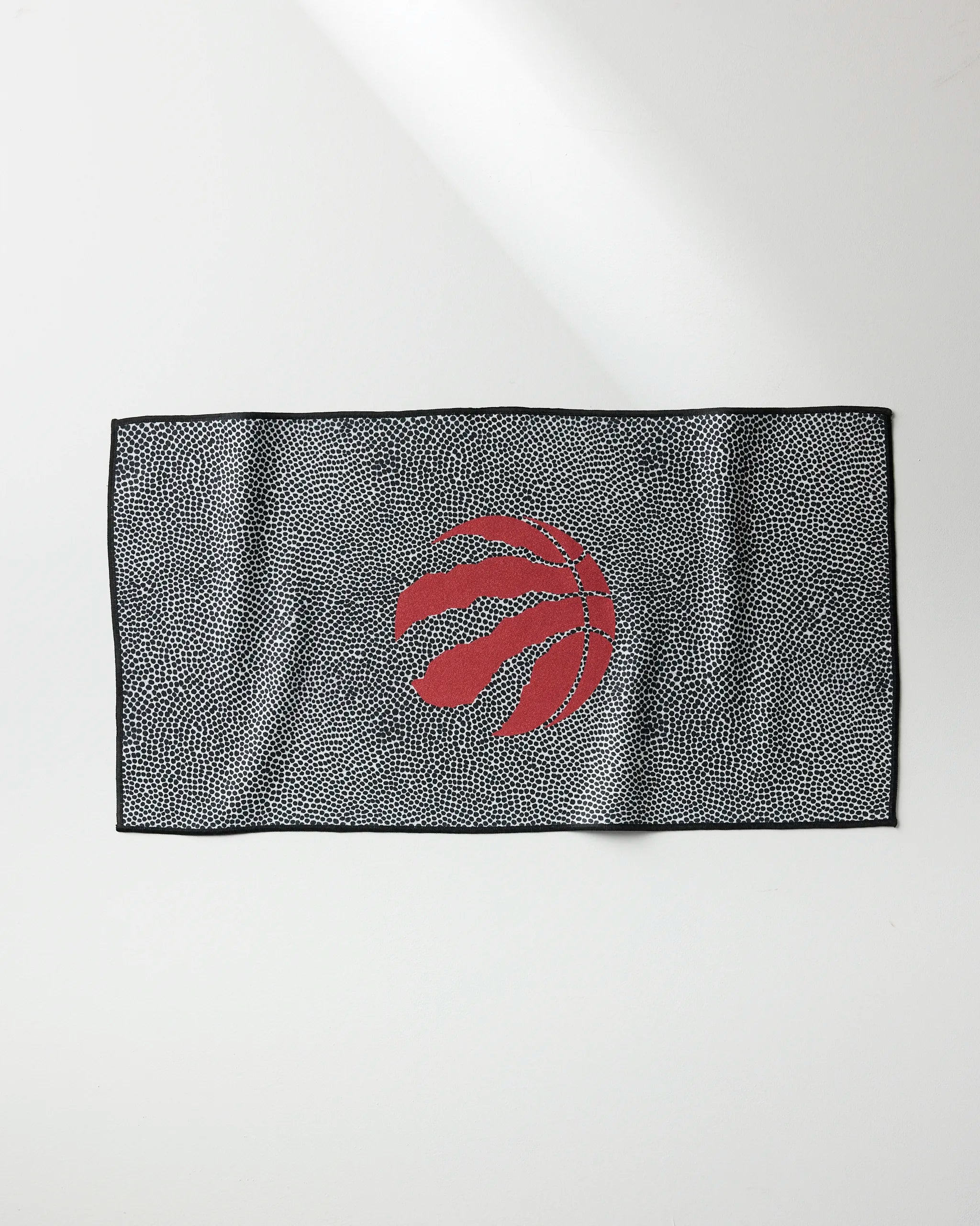 The NBALAB x Geometry Raptors Grip is a rectangular black and white speckled fitness towel, featuring a red stylized basketball with claw marks at the center, shown laid flat on a white surface.
