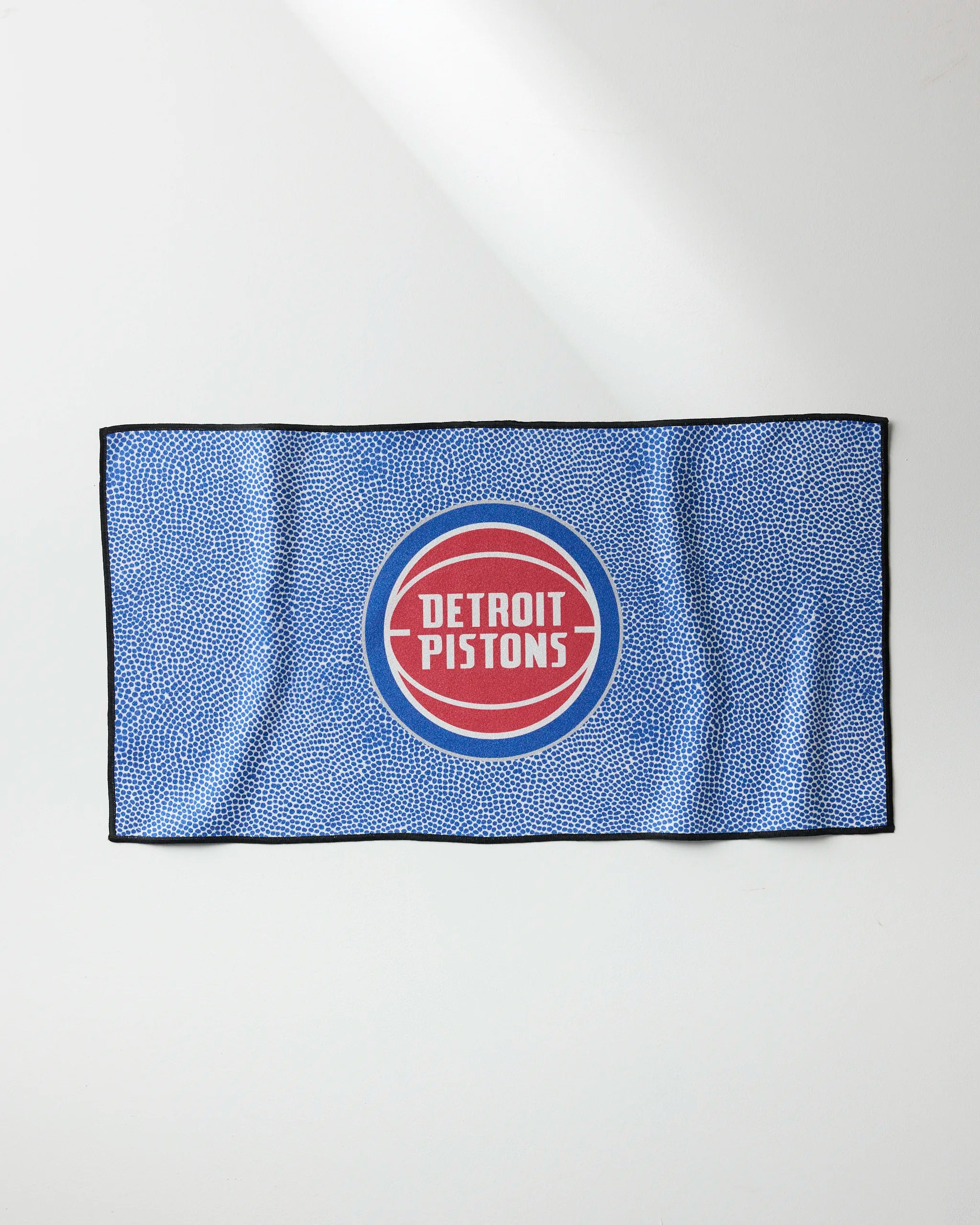 The Pistons Grip by NBALAB x Geometry is a blue quick-drying fitness towel with a textured pattern, black border, and the Detroit Pistons logo—red and white circles with bold white lettering—displayed prominently at the center.
