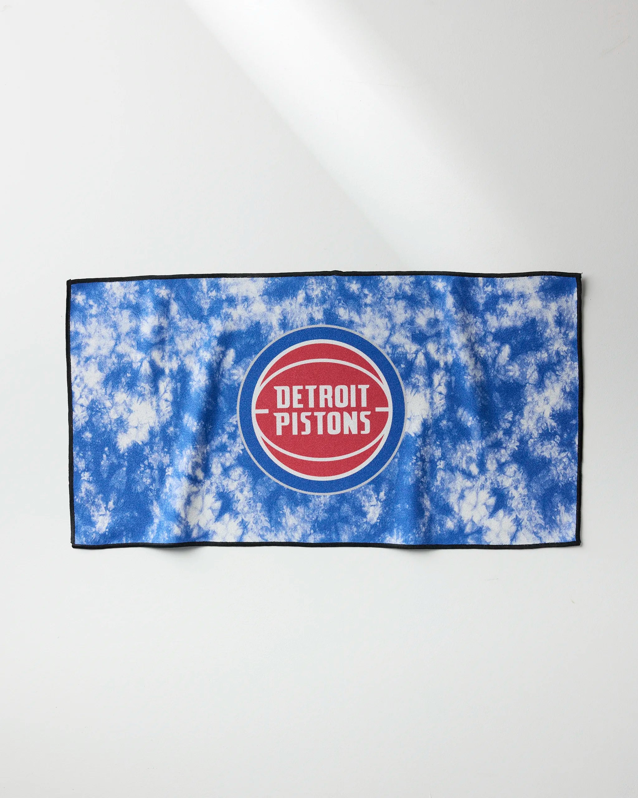 The Pistons Flash fitness towel by NBALAB x Geometry showcases a blue and white tie-dye design with a red and white Detroit Pistons logo in the center, set against a white background.