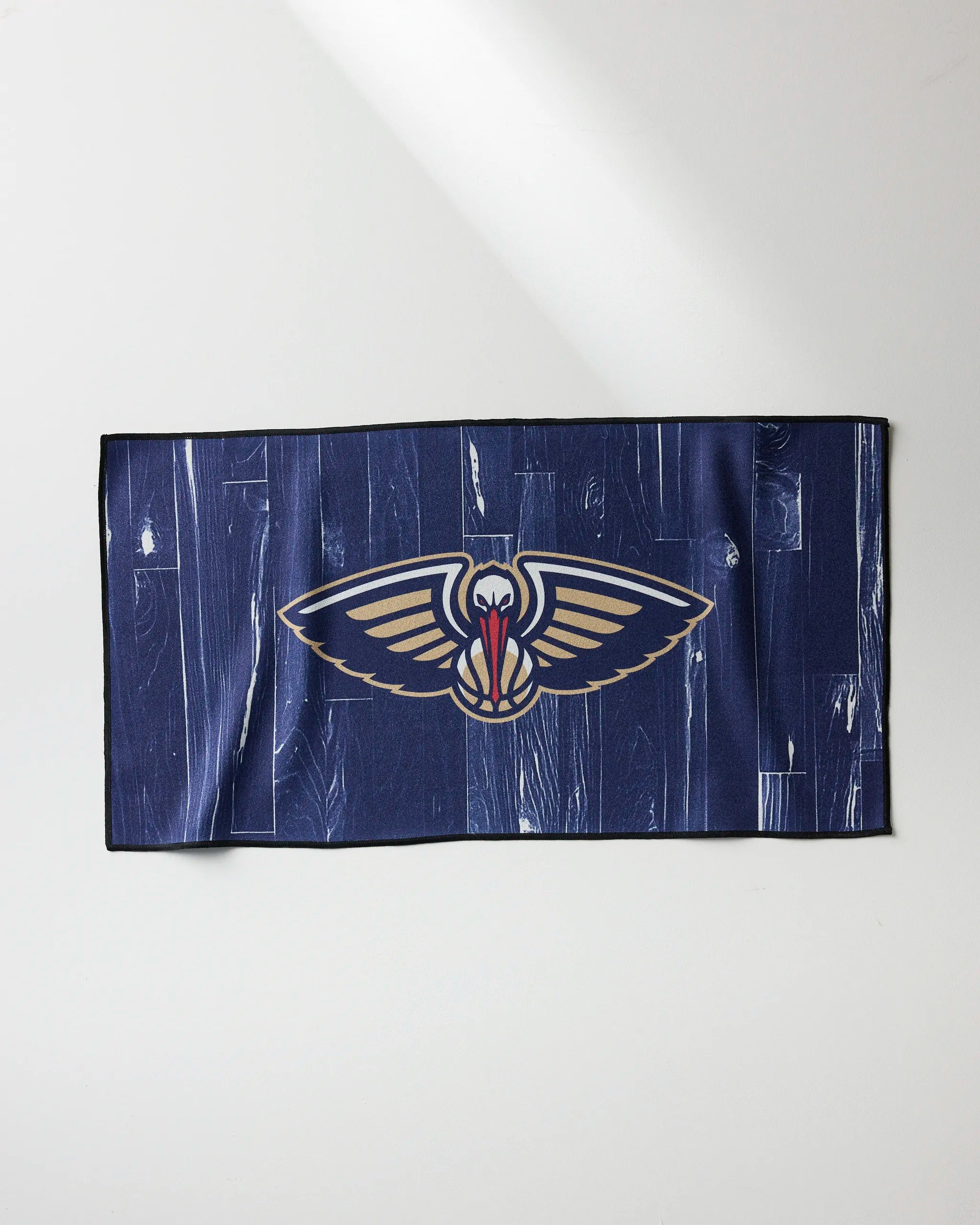 The Pelicans Zone fitness towel by NBALAB x Geometry is navy blue with a bold New Orleans Pelicans logo of a stylized pelican with outstretched wings showcased on a light background.