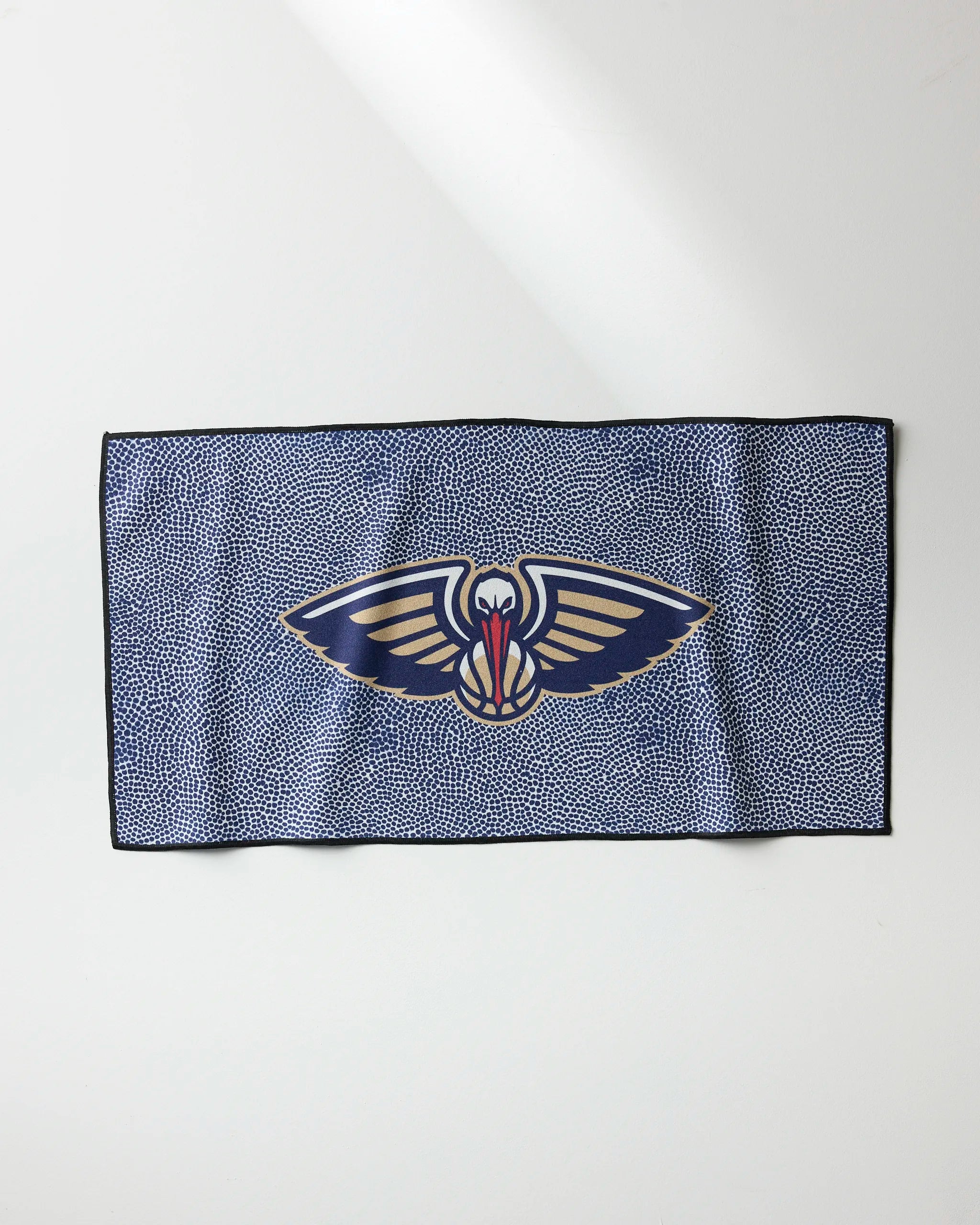 The Pelicans Grip by NBALAB x Geometry is a blue rectangular quick-dry towel with small white dots and the New Orleans Pelicans logo—a stylized pelican with outstretched wings and red crest—centered on the fabric.