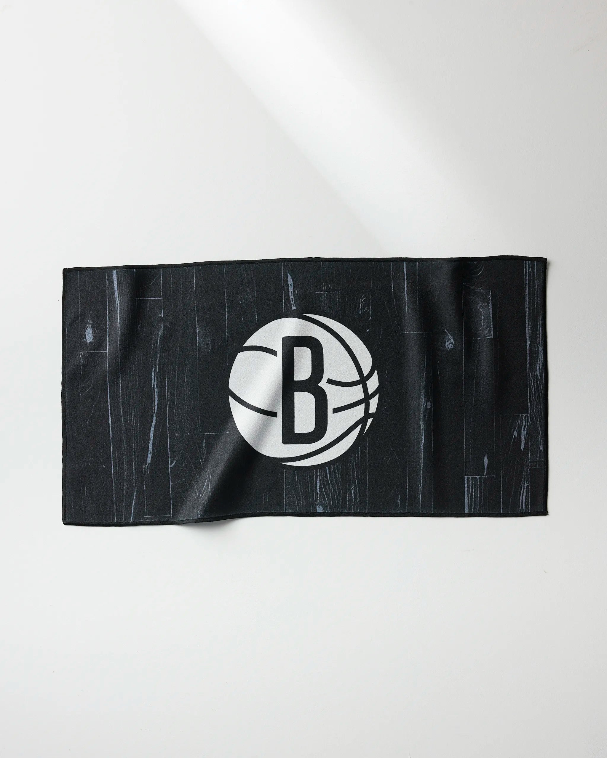 The NBALAB x Geometry Nets Zone towel is a black rectangular NBA fitness towel featuring the Brooklyn Nets logo—a white "B" in a basketball—displayed in the center. The quick-drying towel is laid flat on a white surface.