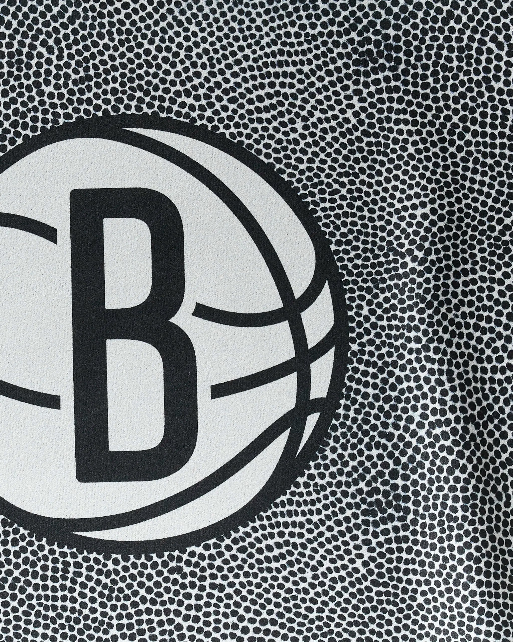 Close-up of the Brooklyn Nets logo—a bold B inside a basketball—set on a dotted black-and-white background. The NBALAB x Geometry Nets Grip is perfect as an NBA fitness towel or sustainable workout towel.