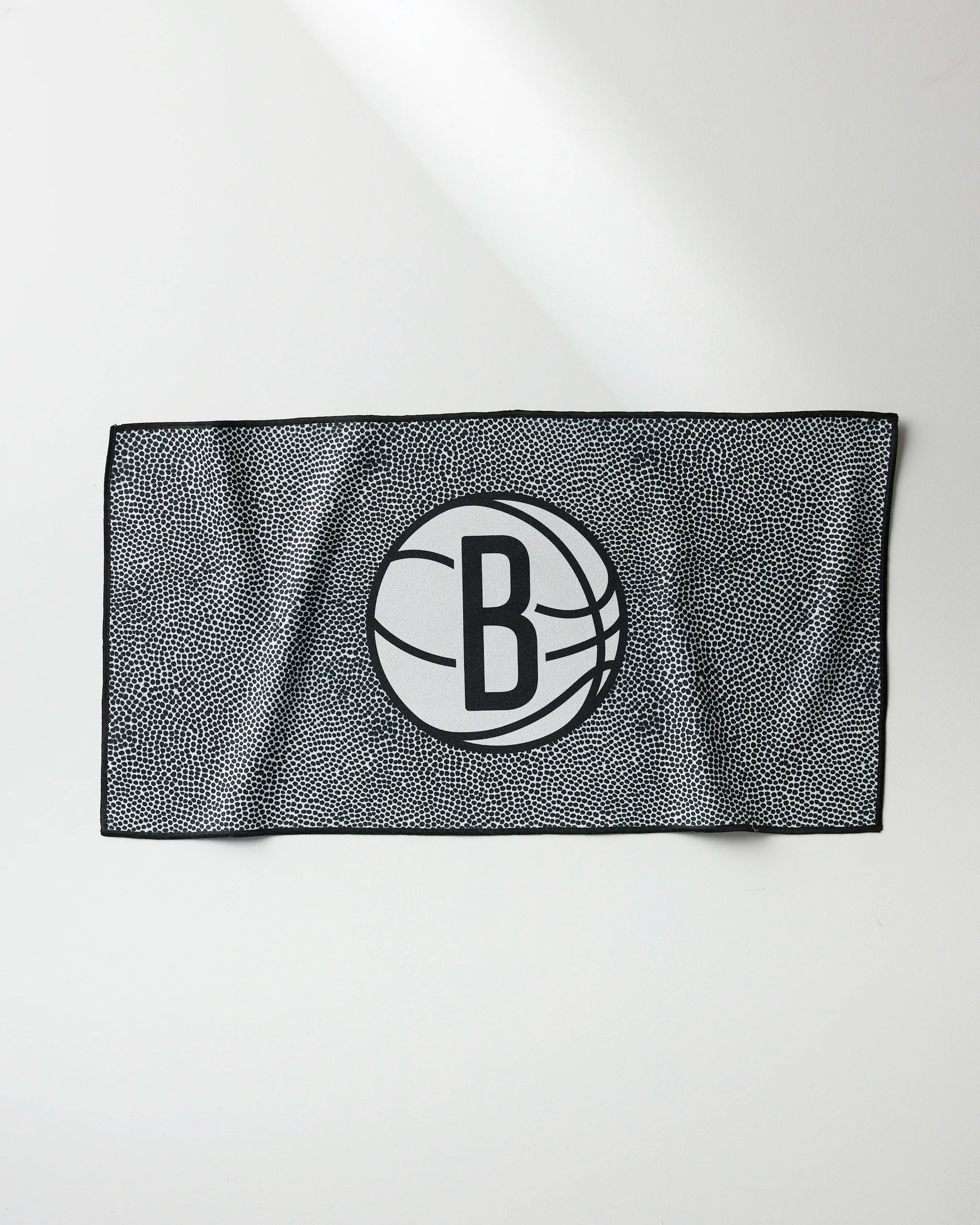 The NBALAB x Geometry Nets Grip is a rectangular, quick-drying gym towel featuring a black-and-white dotted pattern and the bold Brooklyn Nets logo—a B inside a basketball—centered on a plain white background.