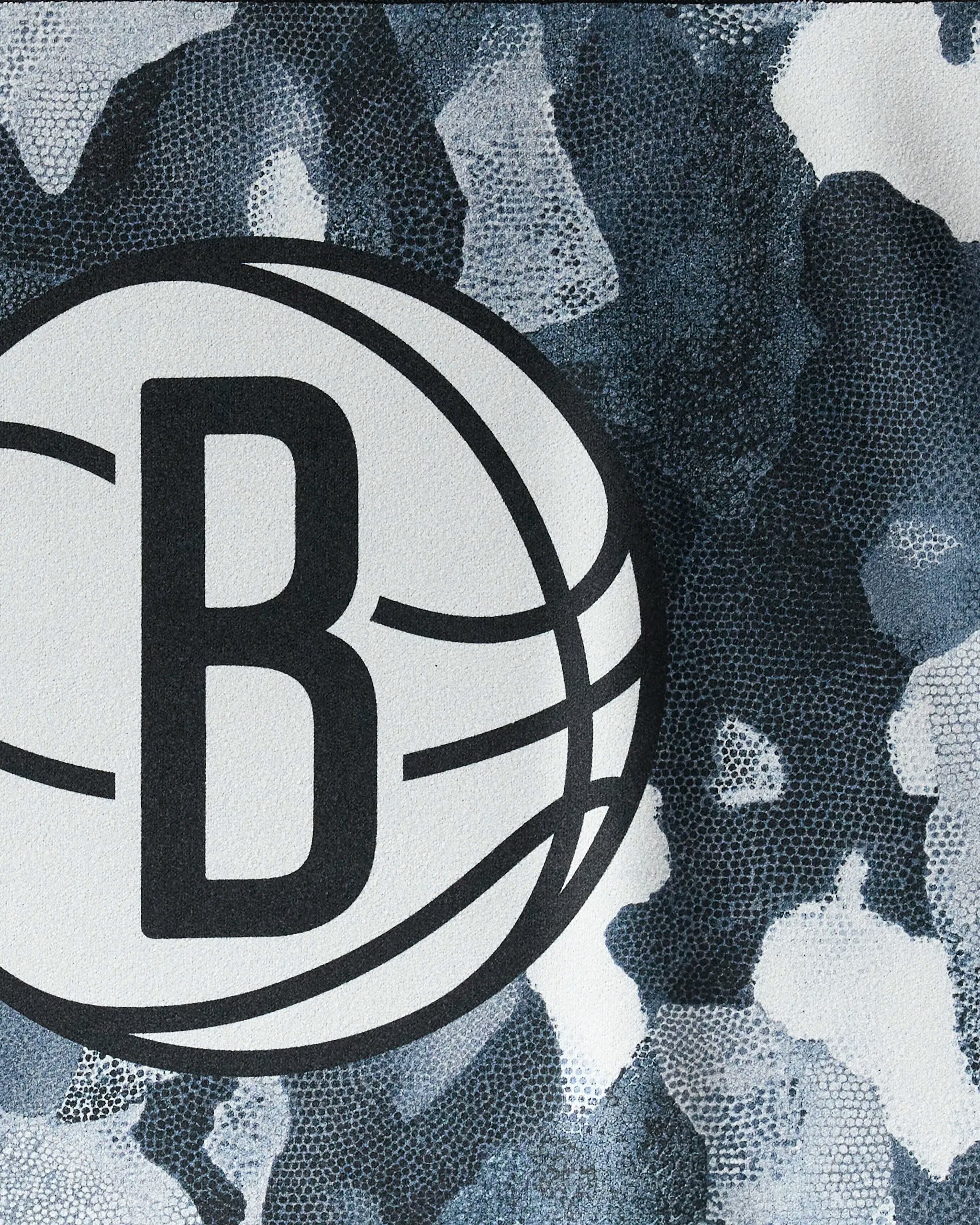A close-up of the Brooklyn Nets logo with a large "B" in a basketball outline on a blue, black, and white camo background—ideal for the NBALAB x Geometry "Nets Camo" NBA fitness or quick-drying gym towel.