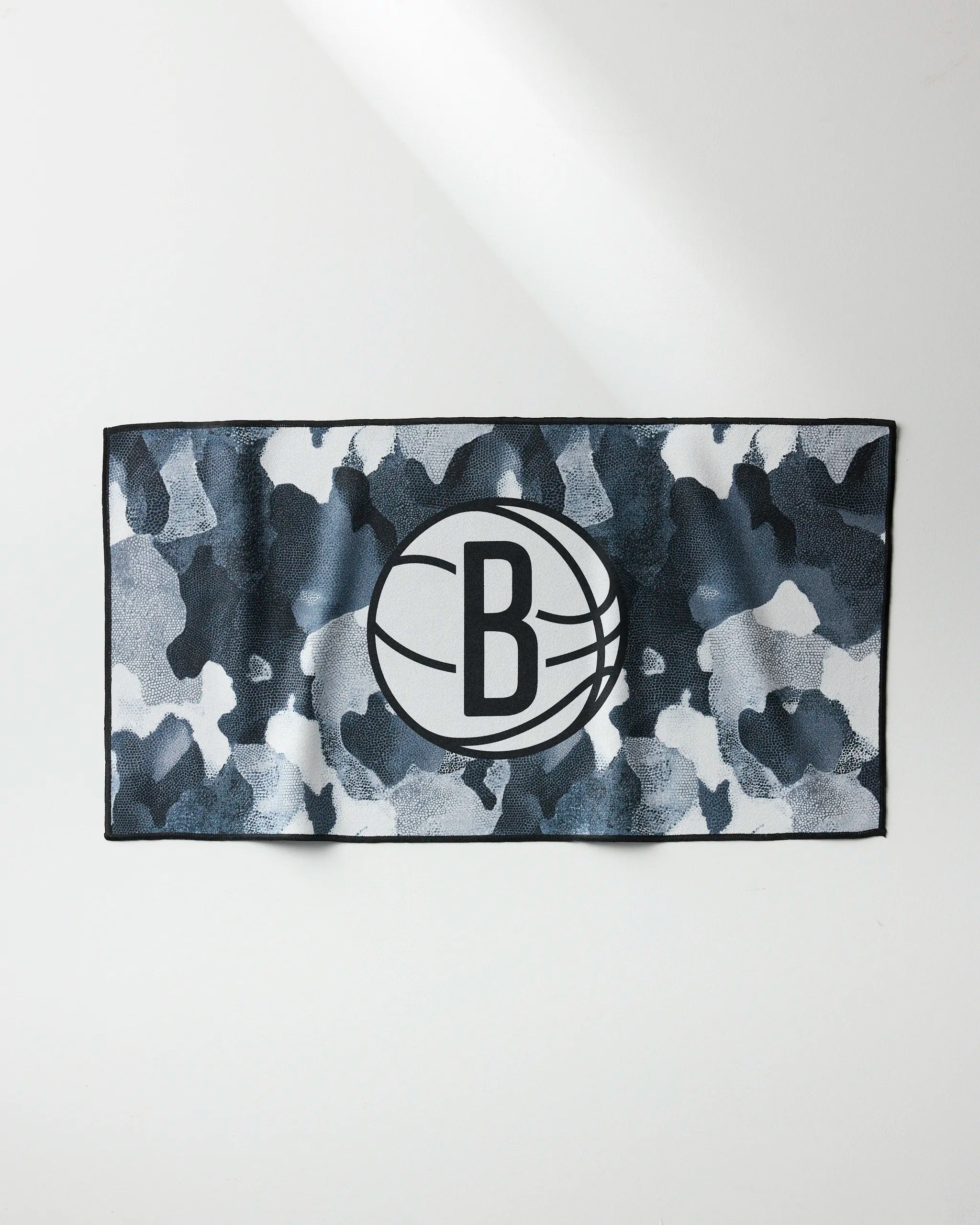 The NBALAB x Geometry Nets Camo towel features a black and gray camo pattern with the Brooklyn Nets “B” basketball logo centered on the front—ideal as a quick-drying gym towel for fans and athletes.