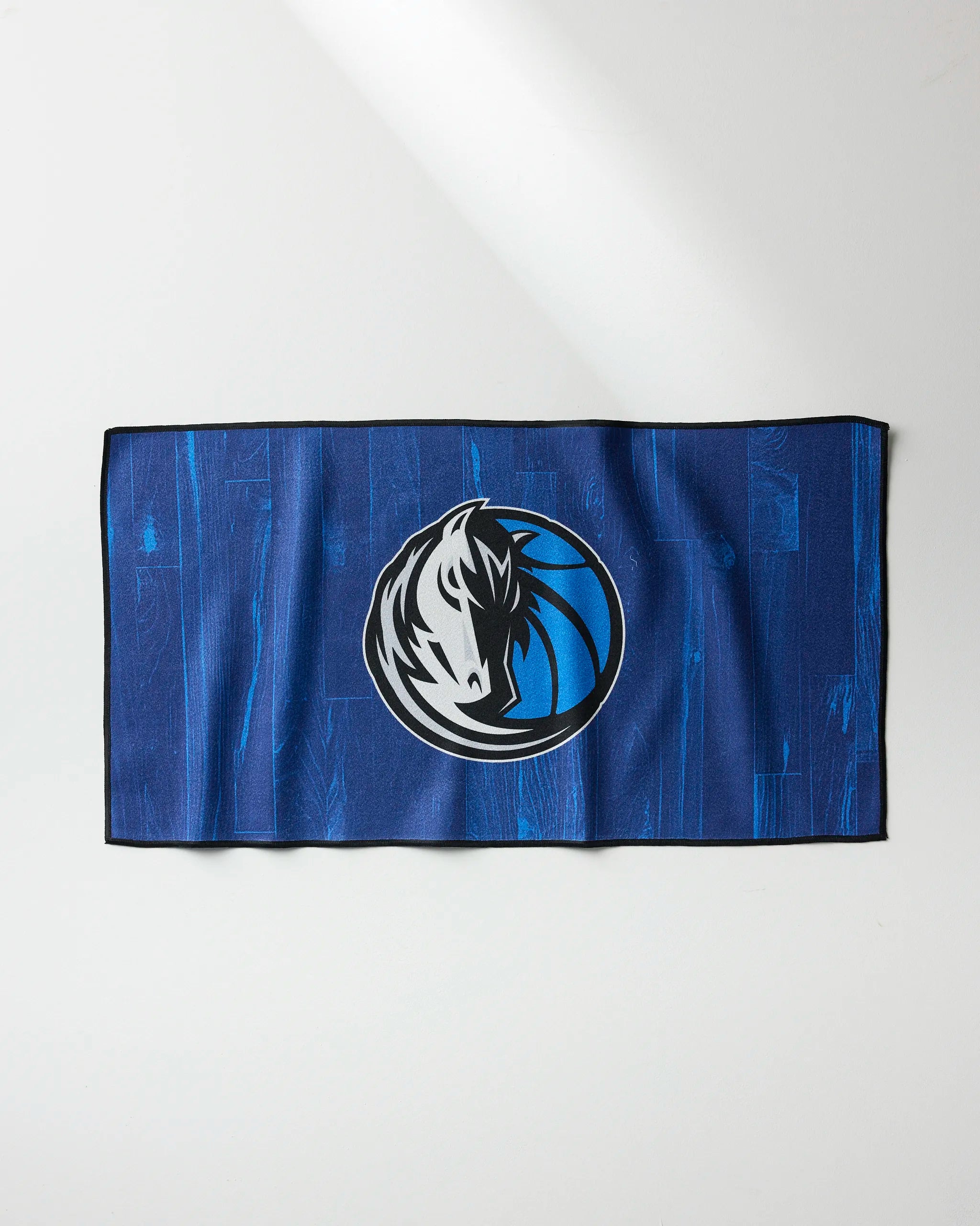 The Mavericks Zone fitness towel by NBALAB x Geometry features a blue design with a stylized Dallas Mavericks horse logo. Laid flat, it’s perfect as a quick-drying gym towel for any fan’s workout routine.