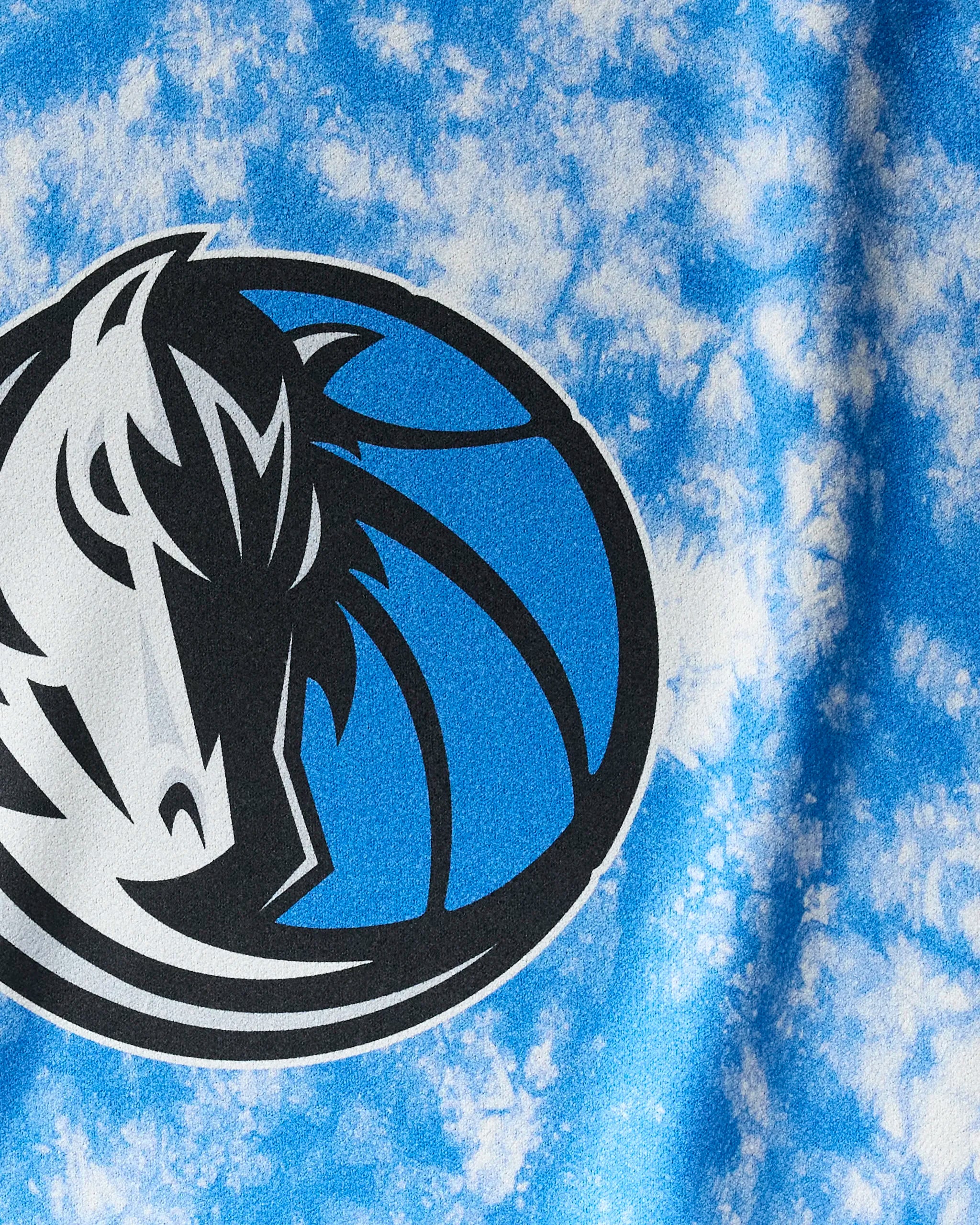 Close-up of the Mavericks Flash towel by NBALAB x Geometry, showing the Dallas Mavericks logo—a stylized horse head on a blue and white ball—printed on blue and white tie-dye Geoweave fabric.