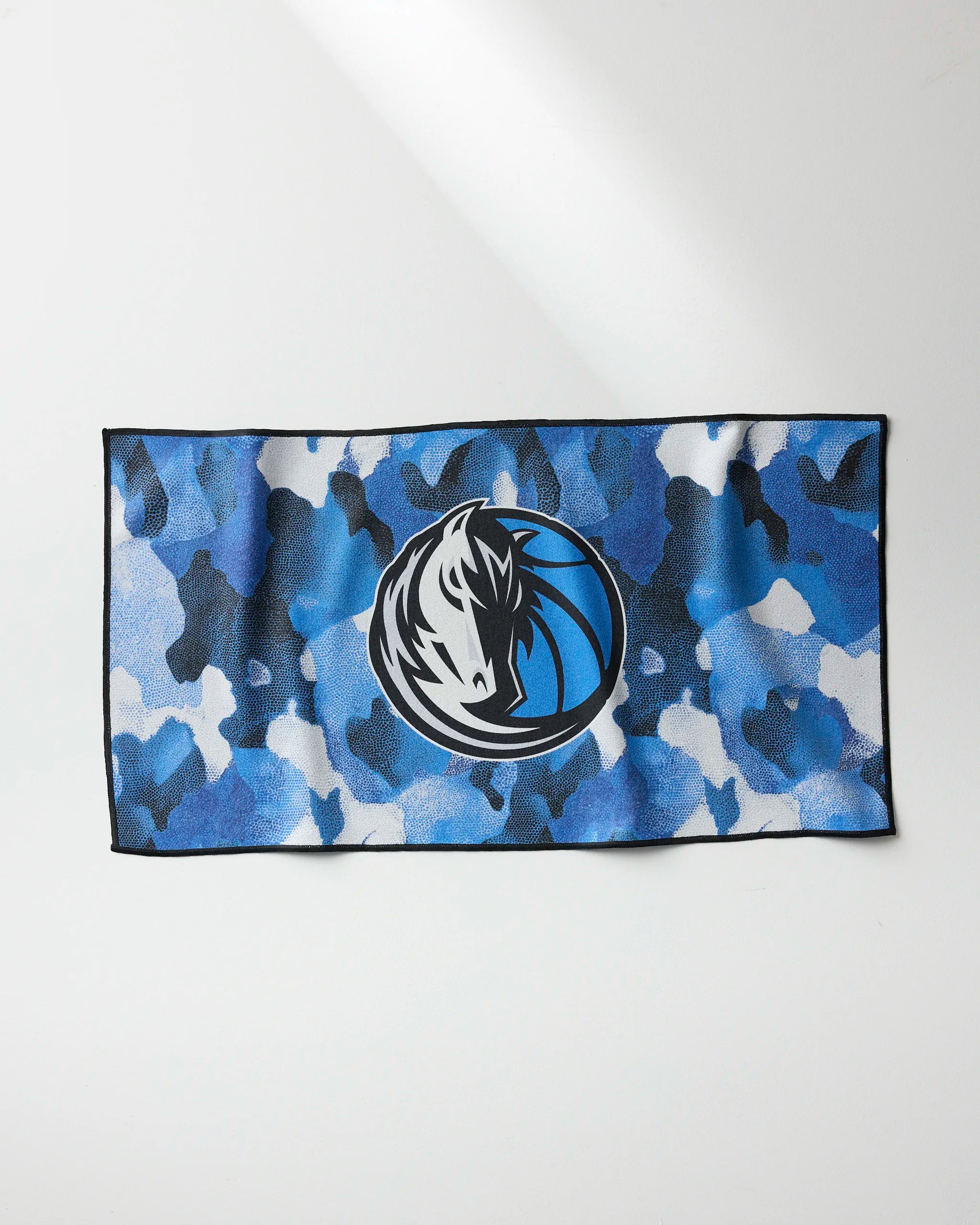 The Mavericks Camo gym towel by NBALAB x Geometry is a rectangular, quick-drying towel with a blue, black, and white camo pattern and the Dallas Mavericks logo in the center, shown laid flat on a white surface.