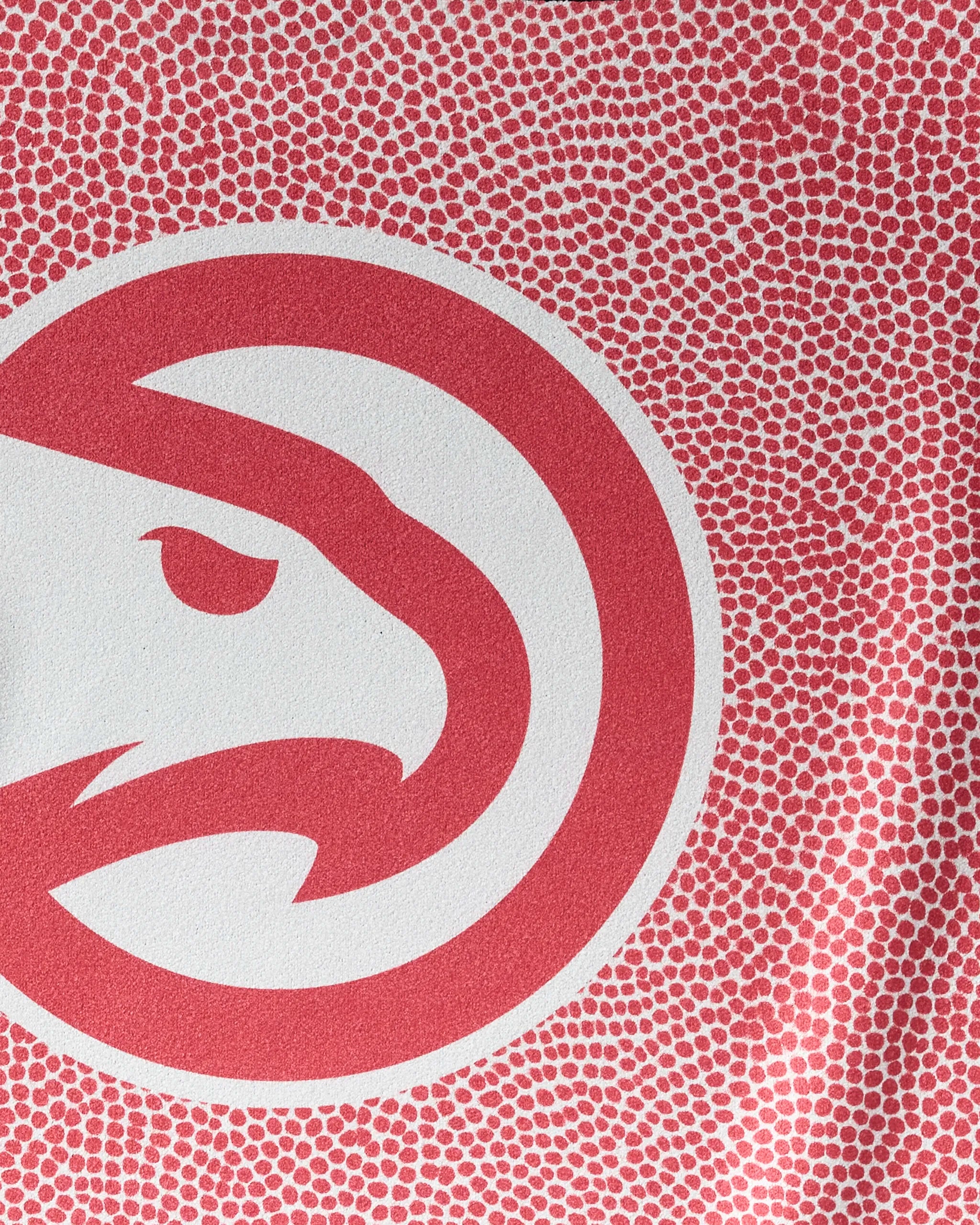 A close-up of the Atlanta Hawks logo—a bold red hawk head in a circular emblem—on a red and white dotted background, featured on the Hawks Grip NBA fitness towel by NBALAB x Geometry.