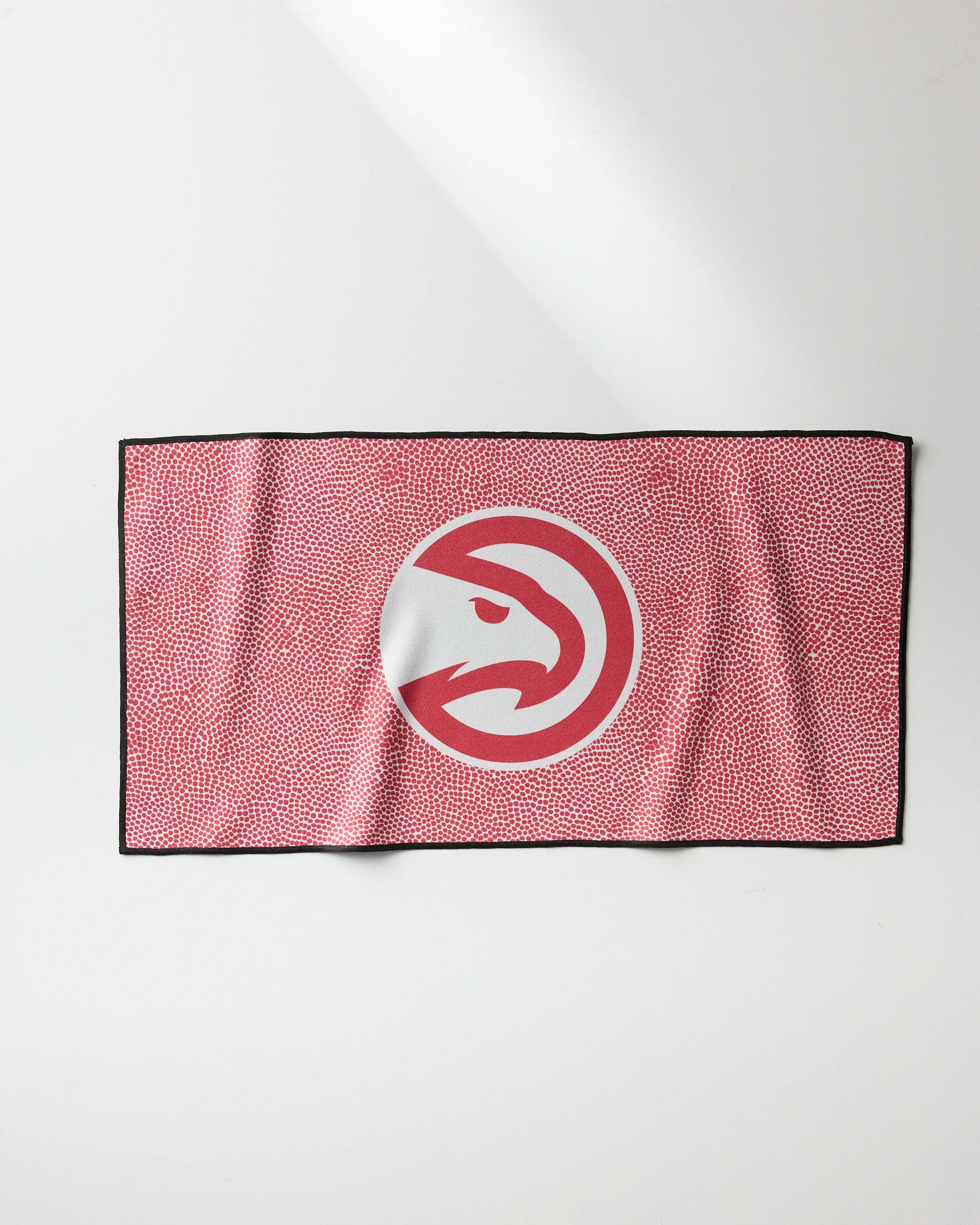 The Hawks Grip by NBALAB x Geometry is a rectangular NBA fitness towel featuring the Atlanta Hawks logo on a red and white patterned background with a black border, shown laid flat on a white surface.