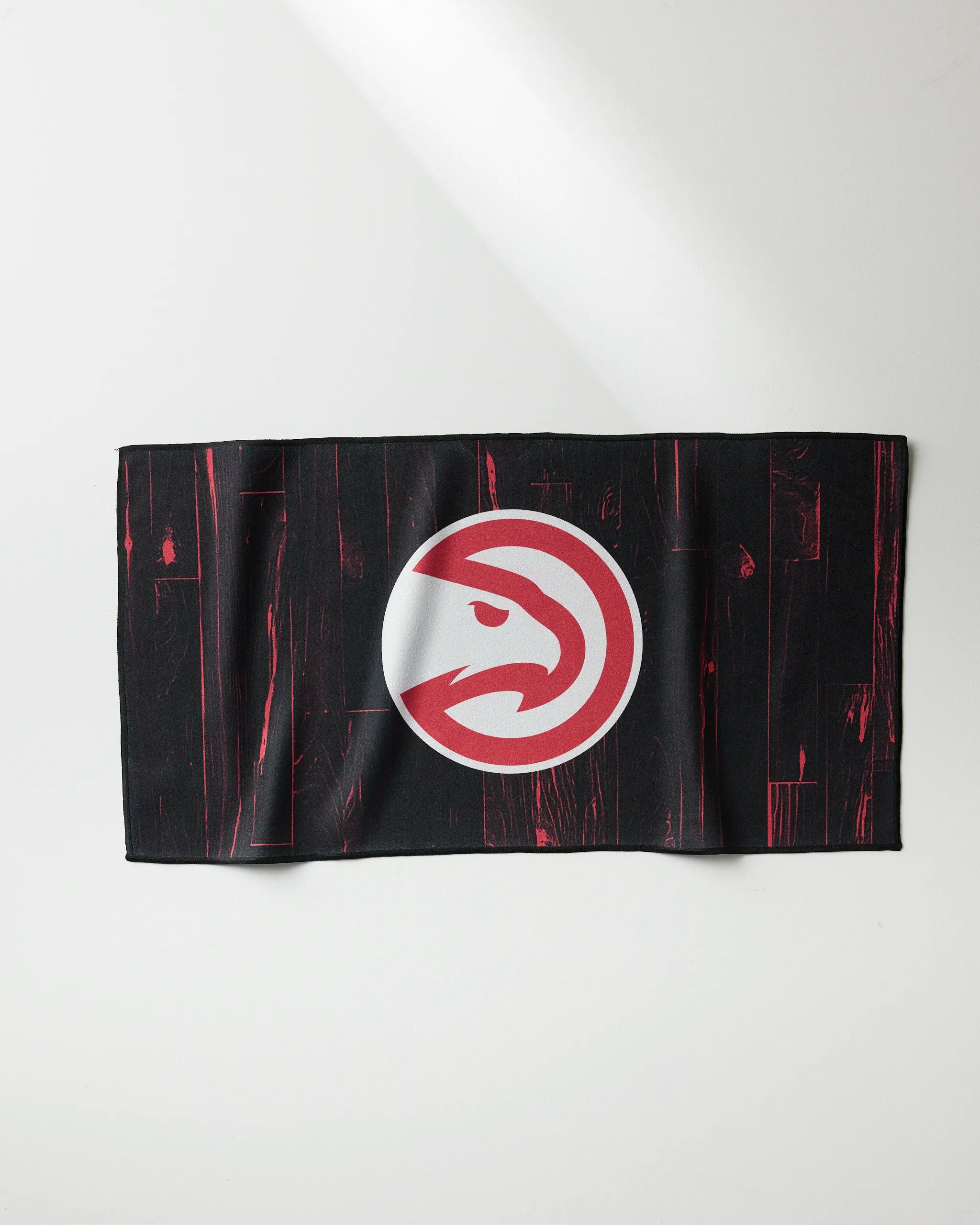 The Hawks Zone towel by NBALAB x Geometry features a black rectangular design with red streaks and a bold white and red Atlanta Hawks logo at the center, displayed flat on a white surface.