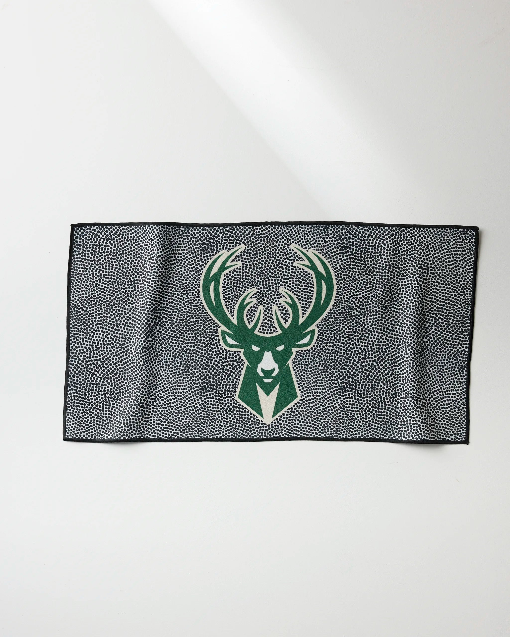 The NBALAB x Geometry Bucks Grip is a rectangular fitness towel with a green and white deer head logo centered on a black and white dotted background, shown on a plain white surface.