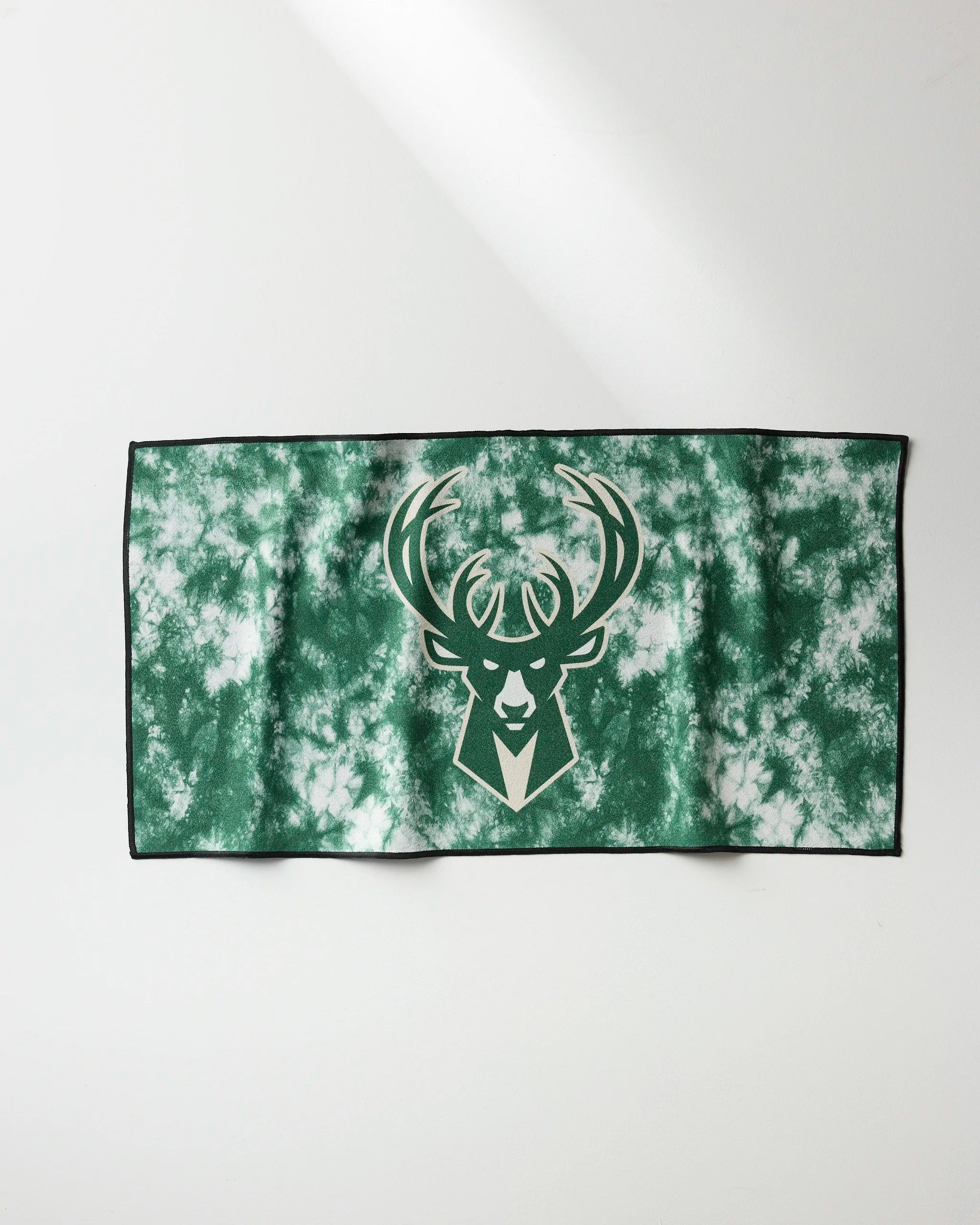 The NBALAB x Geometry Bucks Flash is a green and white tie-dye NBA fitness towel featuring the Milwaukee Bucks deer head logo in the center, shown lying flat on a white surface.