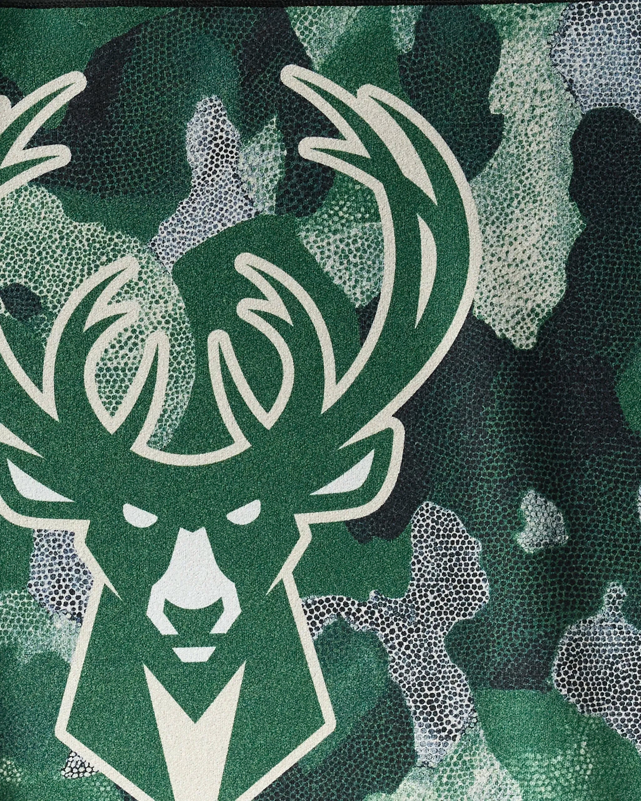 The Bucks Camo towel by NBALAB x Geometry features a stylized green and white deer head logo with large antlers over a green, black, and white camo background—ideal for sustainable NBA workouts.