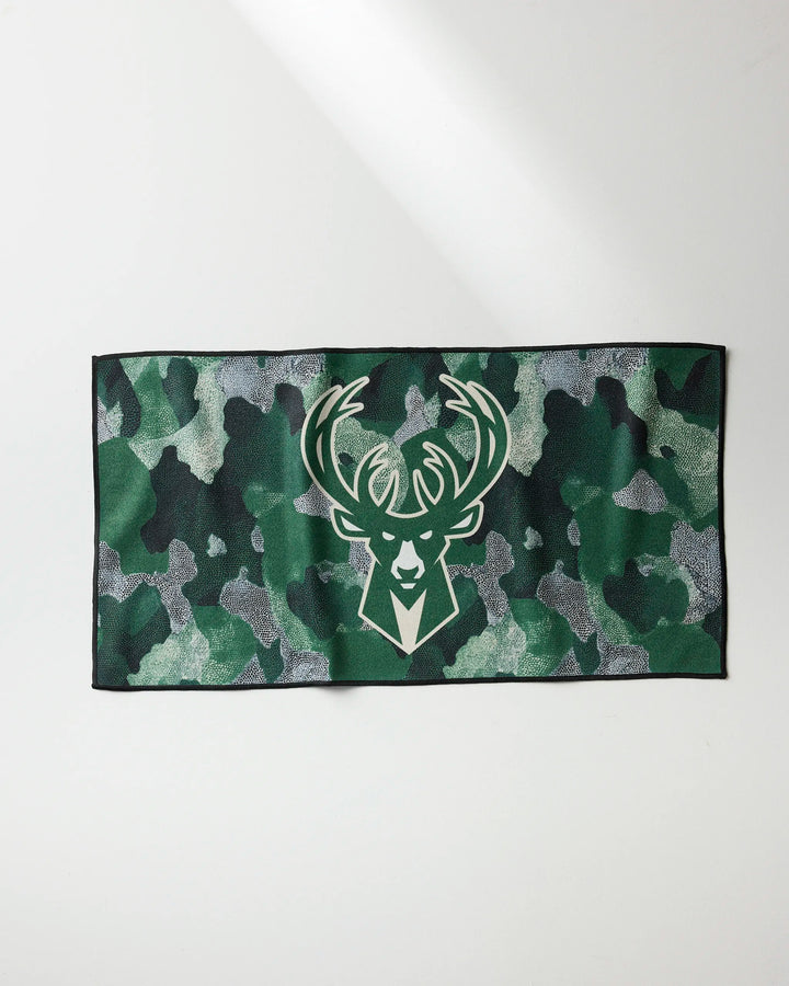 The NBALAB x Geometry "Bucks Camo" is a rectangular NBA fitness towel featuring a green camouflage pattern and the Milwaukee Bucks deer head logo centered, displayed on a light surface.