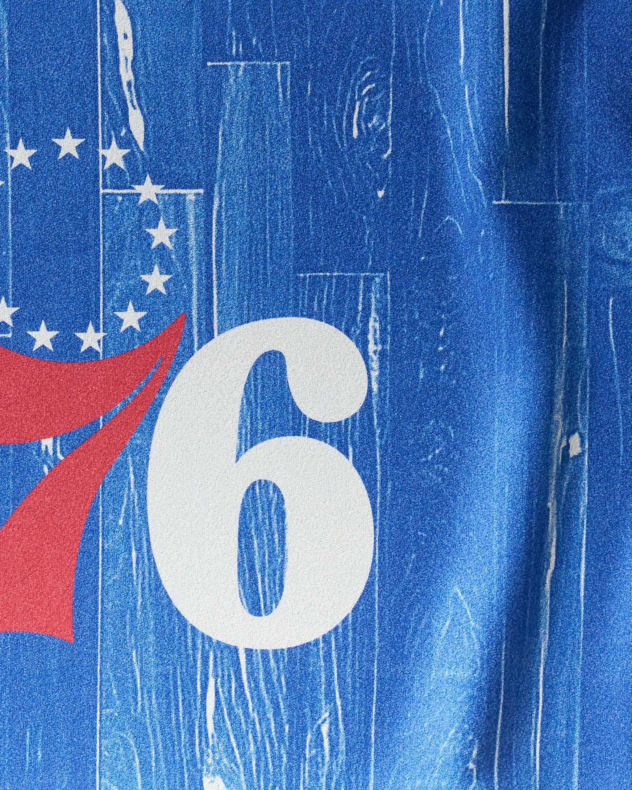 Close-up of the NBALAB x Geometry 76ers Zone towel, featuring part of the white "76" logo on a textured blue, wood-like background with white stars in the upper left—ideal for any Philadelphia basketball fan.