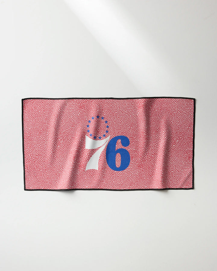 The 76ers Grip by NBALAB x Geometry is a rectangular NBA fitness towel with a red and white dotted design, featuring the number 76 in blue and white plus 13 blue stars above the 7—honoring the Philadelphia 76ers basketball team.