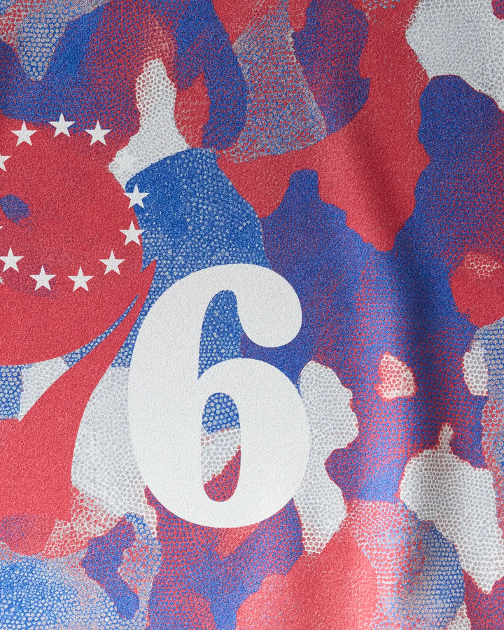 The image shows a close-up of the 76ers Camo gym towel by NBALAB x Geometry, featuring a red, blue, and white camouflage design with a large white number 6 and white stars forming a partial semicircle to its left.