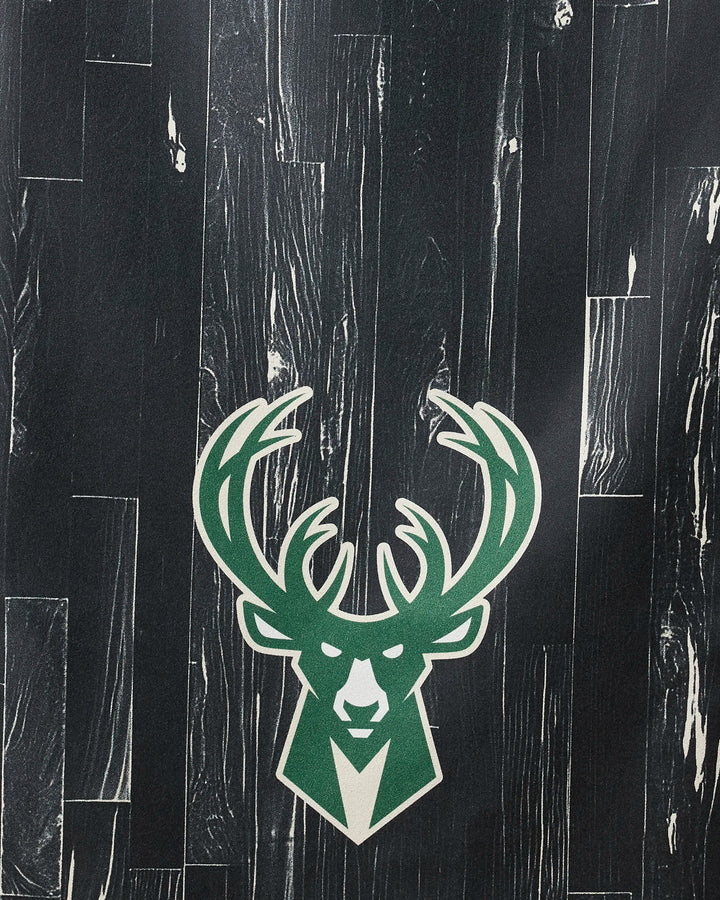 The Bucks Zone towel by NBALAB x Geometry features a bold green and white deer head logo with large antlers, centered against a dark wood-patterned background, bringing NBA-inspired style to your beach days.