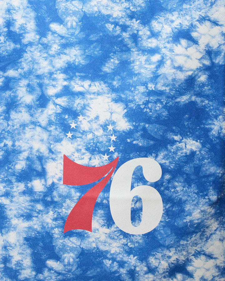 The NBALAB x Geometry 76ers Flash beach towel features a blue and white tie-dye design with a red and white 76 logo and thirteen stars, making it perfect for showcasing team pride while staying dry at the shore.