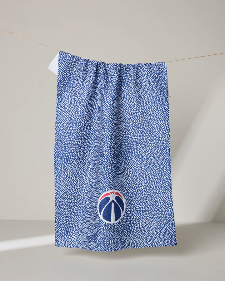 A blue and white textured Wizards Grip tea towel by NBALAB x Geometry hangs on a line against a plain background, featuring a small round logo near the bottom with a stylized red, white, and blue basketball.