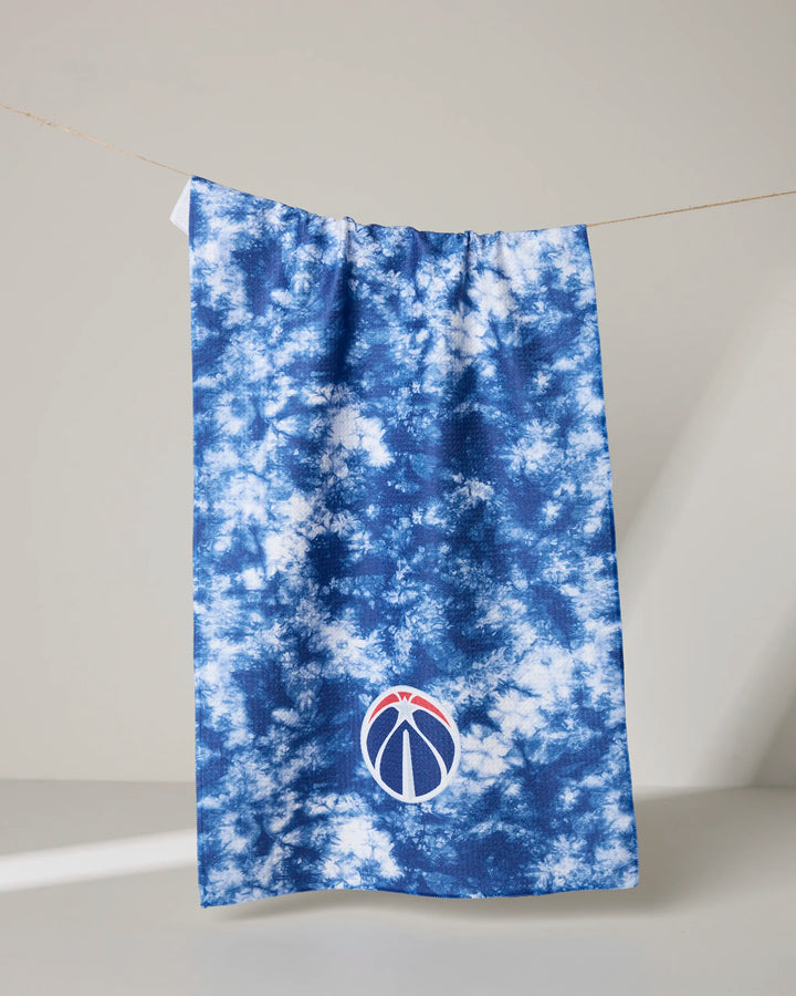 A blue and white tie-dye NBALAB x Geometry "Wizards Flash" tea towel hangs on a line, featuring a small embroidered blue basketball with a red accent near the bottom edge.
