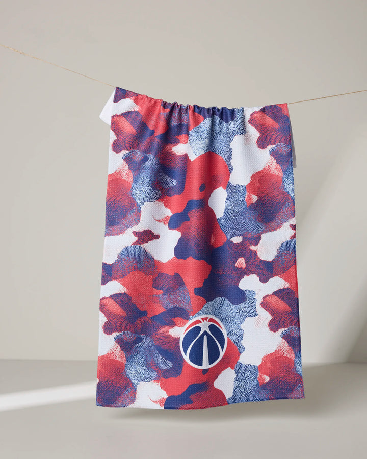 The NBALAB x Geometry Wizards Camo tea towel, featuring a red, white, and blue camouflage pattern with a circular basketball logo, hangs on a line against a neutral background.