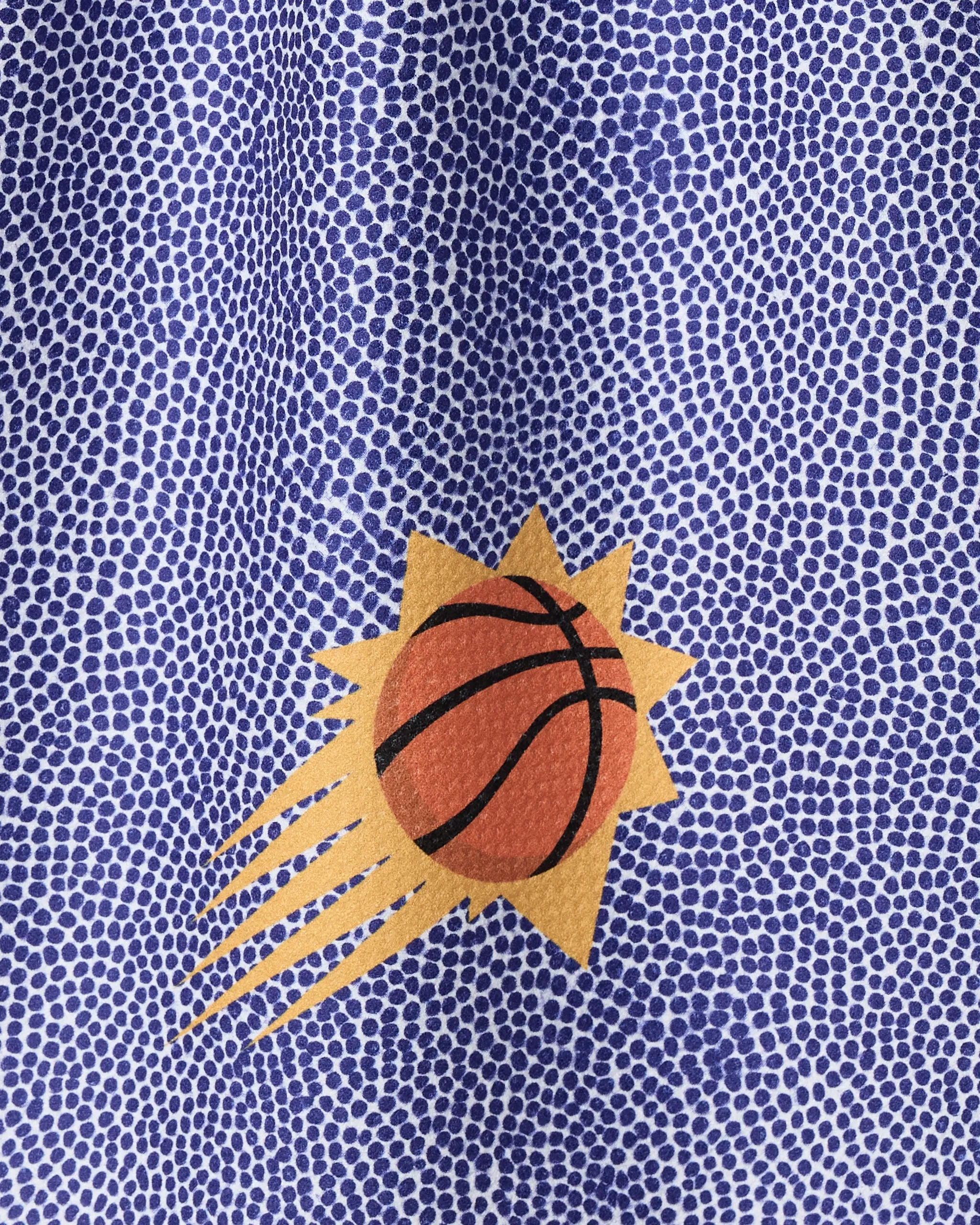 A close-up of the Suns Grip towel by NBALAB x Geometry, showcasing the Phoenix Suns logo with an orange basketball, black lines, yellow sun rays, and a blue and white dotted background.