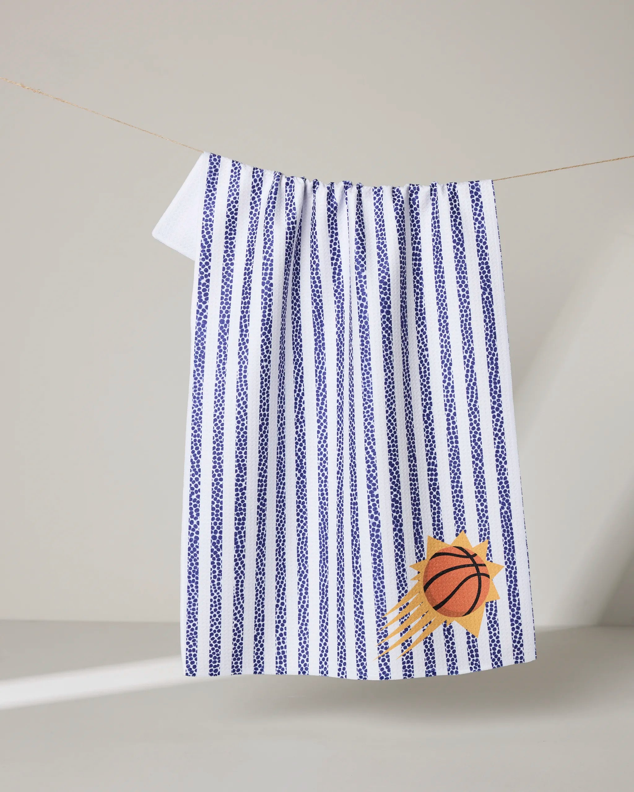 The NBALAB x Geometry Suns Grip Stripe tea towel features vertical blue stripes on white and an orange basketball with motion lines in the corner, making it a stylish, sustainable kitchen towel for basketball fans.
