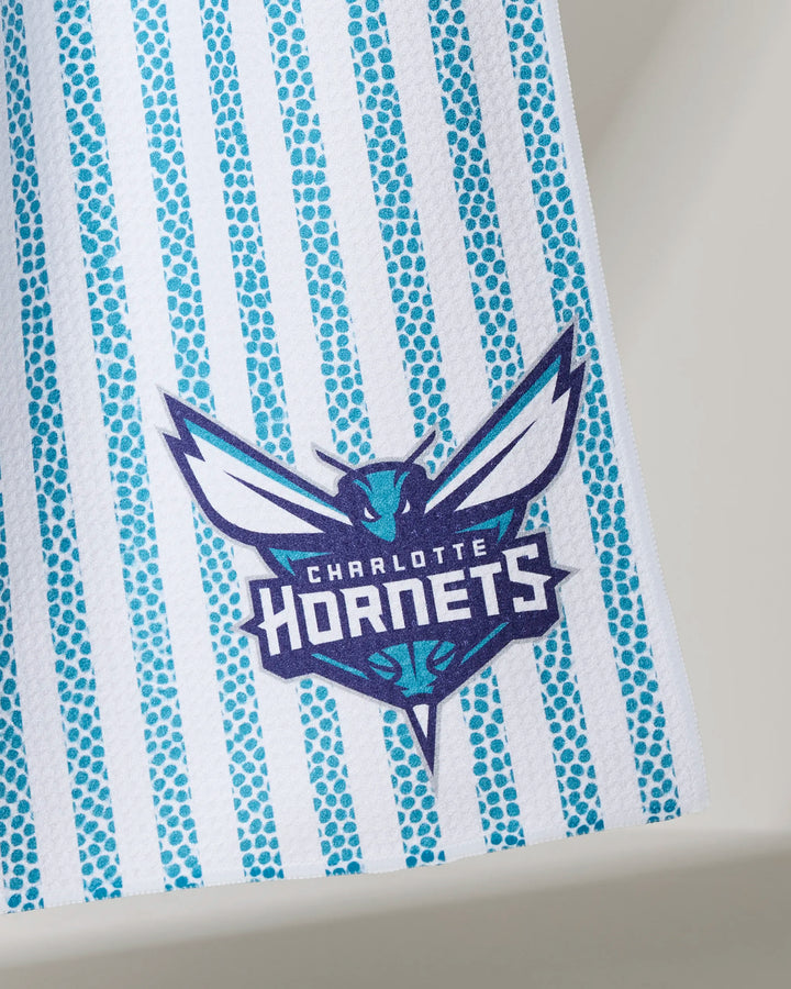 The Hornets Grip Stripe kitchen towel by NBALAB x Geometry features vertical blue dotted stripes and the Charlotte Hornets logo—ideal for NBA fans who value both style and sustainability.