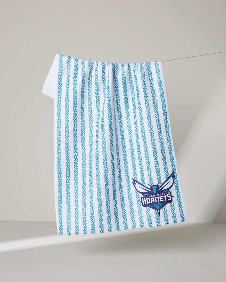 The Hornets Grip Stripe tea towel by NBALAB x Geometry features vertical teal stripes and the Charlotte Hornets logo in teal, purple, and white—a stylish kitchen upgrade for any fan.