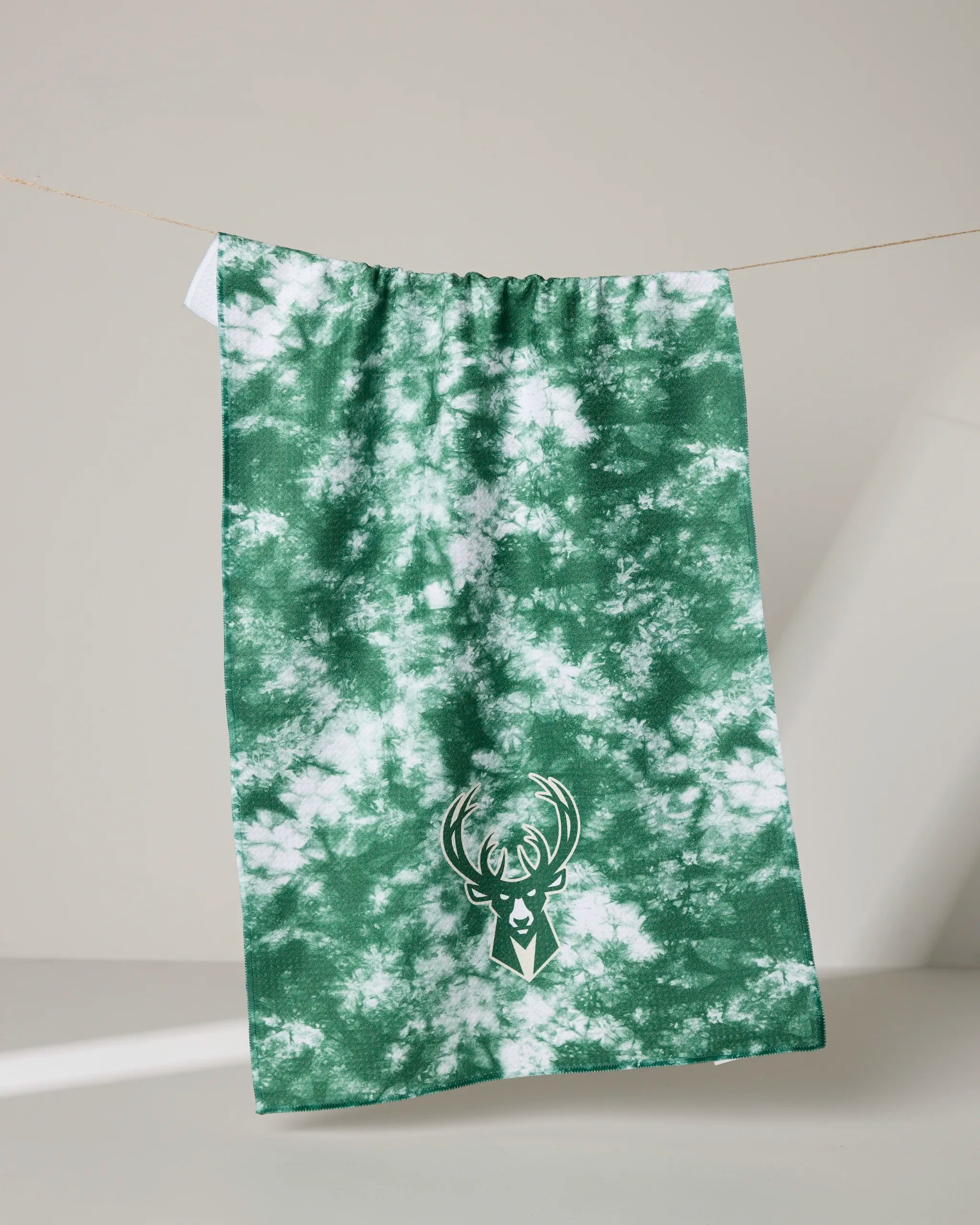 The Bucks Flash tea towel by NBALAB x Geometry features a green and white tie-dye design with the Milwaukee Bucks deer head logo in white, perfect for adding sustainable style to any fan's kitchen.